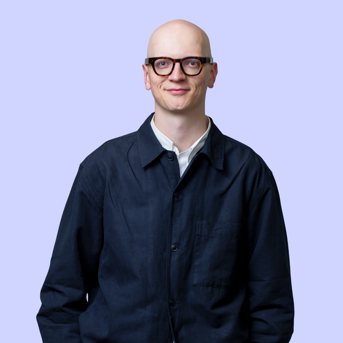 Caspar wearing glasses and a denim shirt, sitting against an orange background.