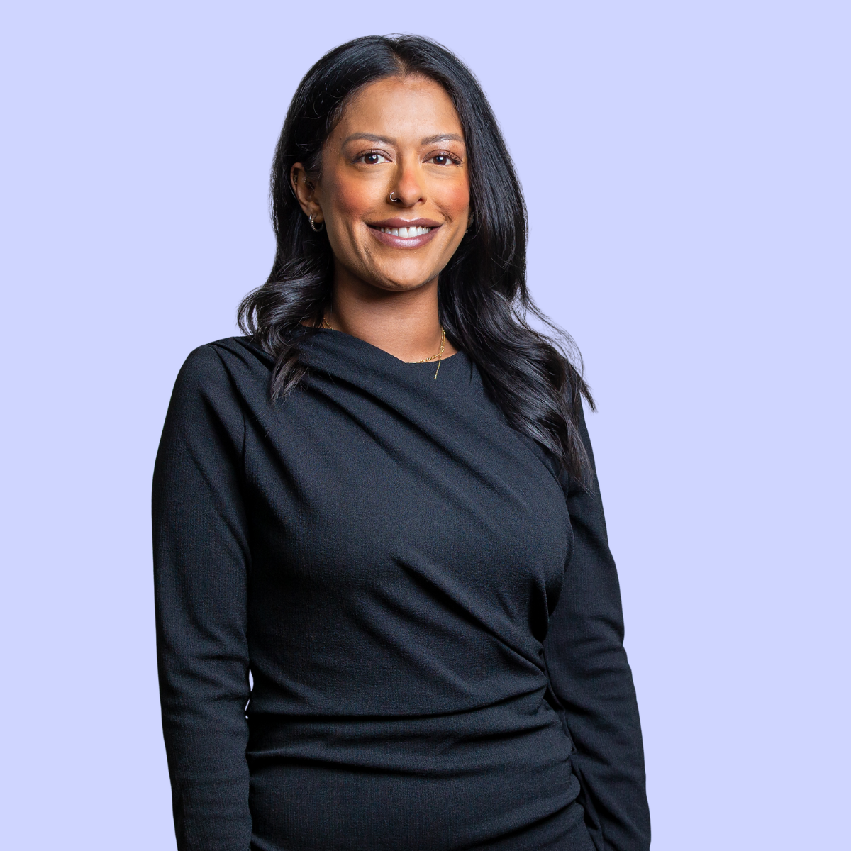 Sheliza with long hair in brown long-sleeve shirt, crossing arms, against a peach background.