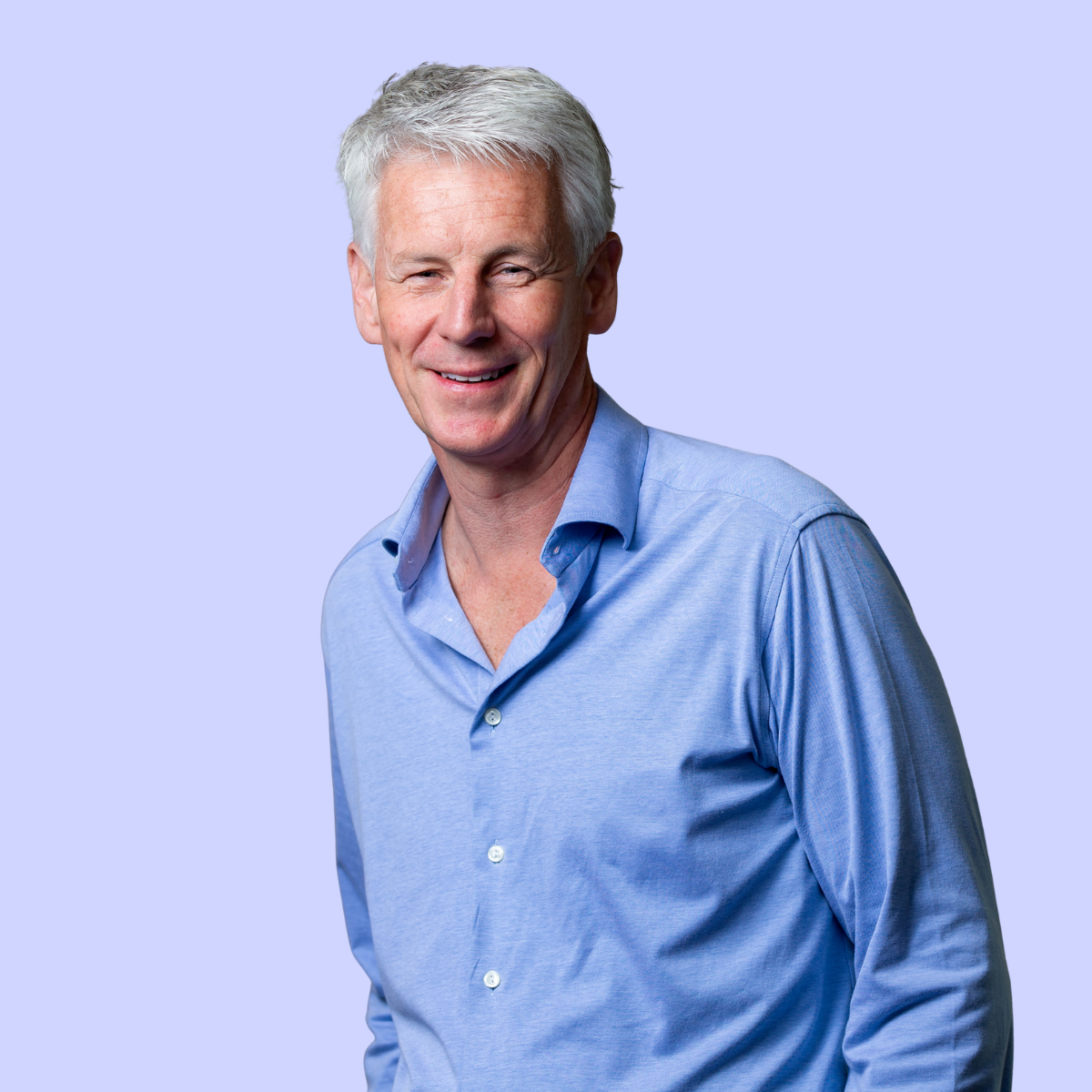 A man with short gray hair wearing a light blue shirt against a purple background.