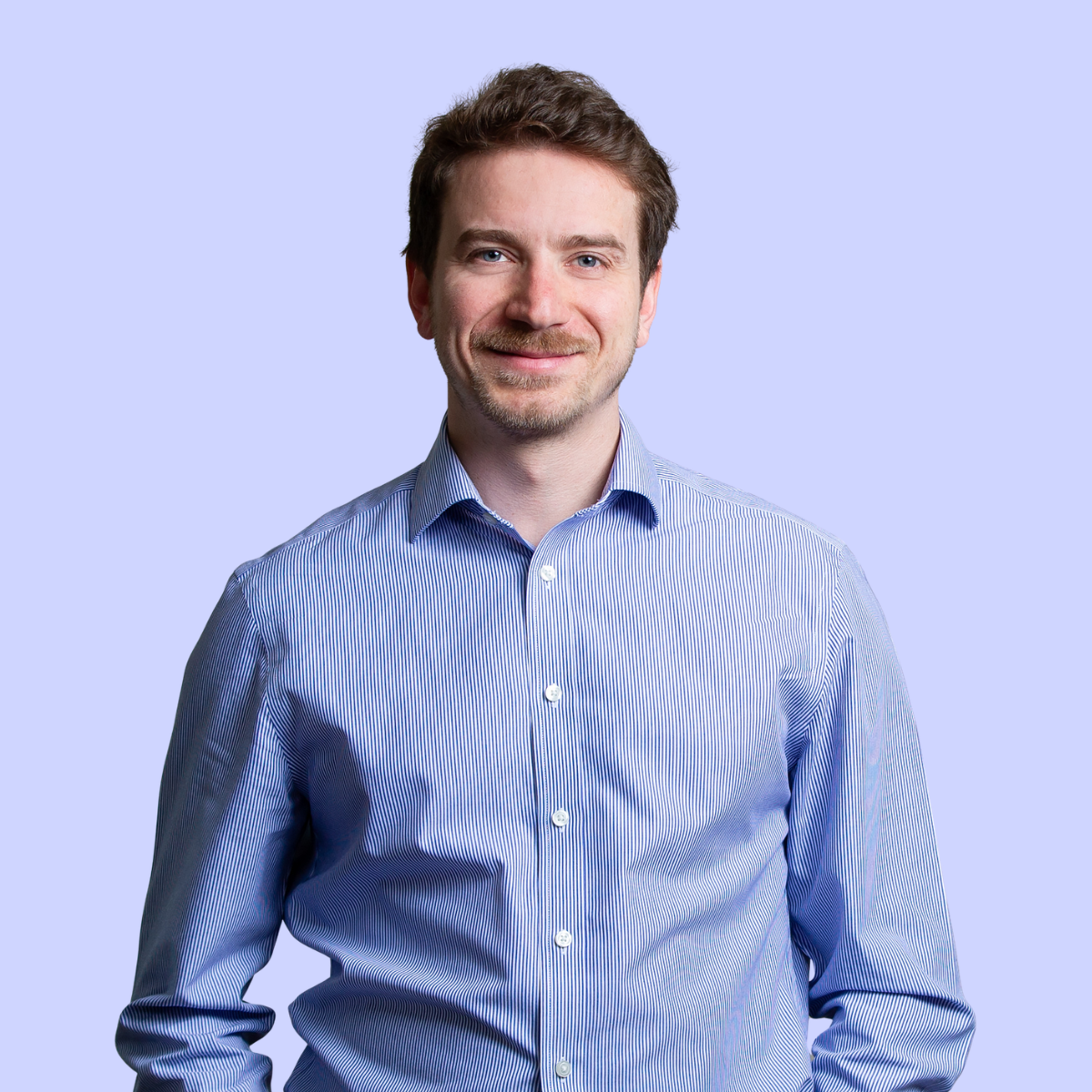 Nick in a dark sweater smiling against a light purple background.