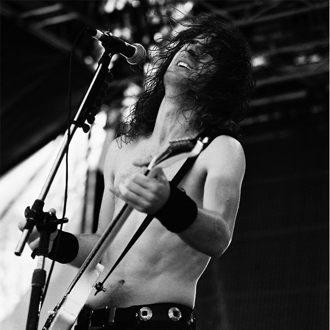 Singer and guitarist performing on stage, playing electric guitar and singing into a microphone.