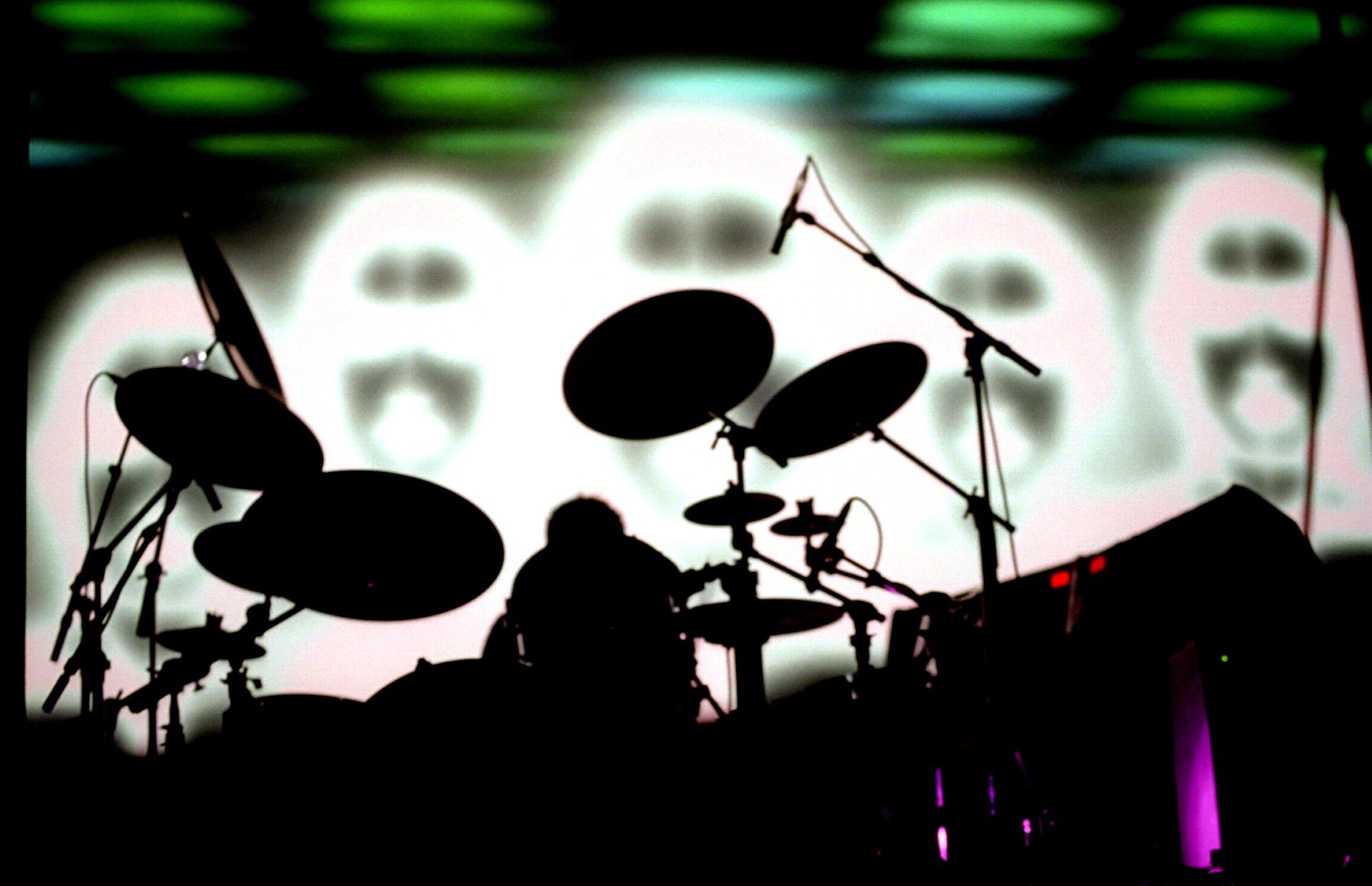 Silhouette of a drum set and drummer in front of a colorful, abstract background.