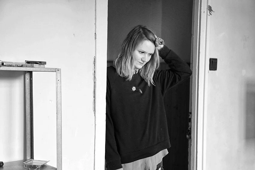Black and white photo of a person standing in a doorway, wearing a dark sweatshirt, with their hand touching their head.
