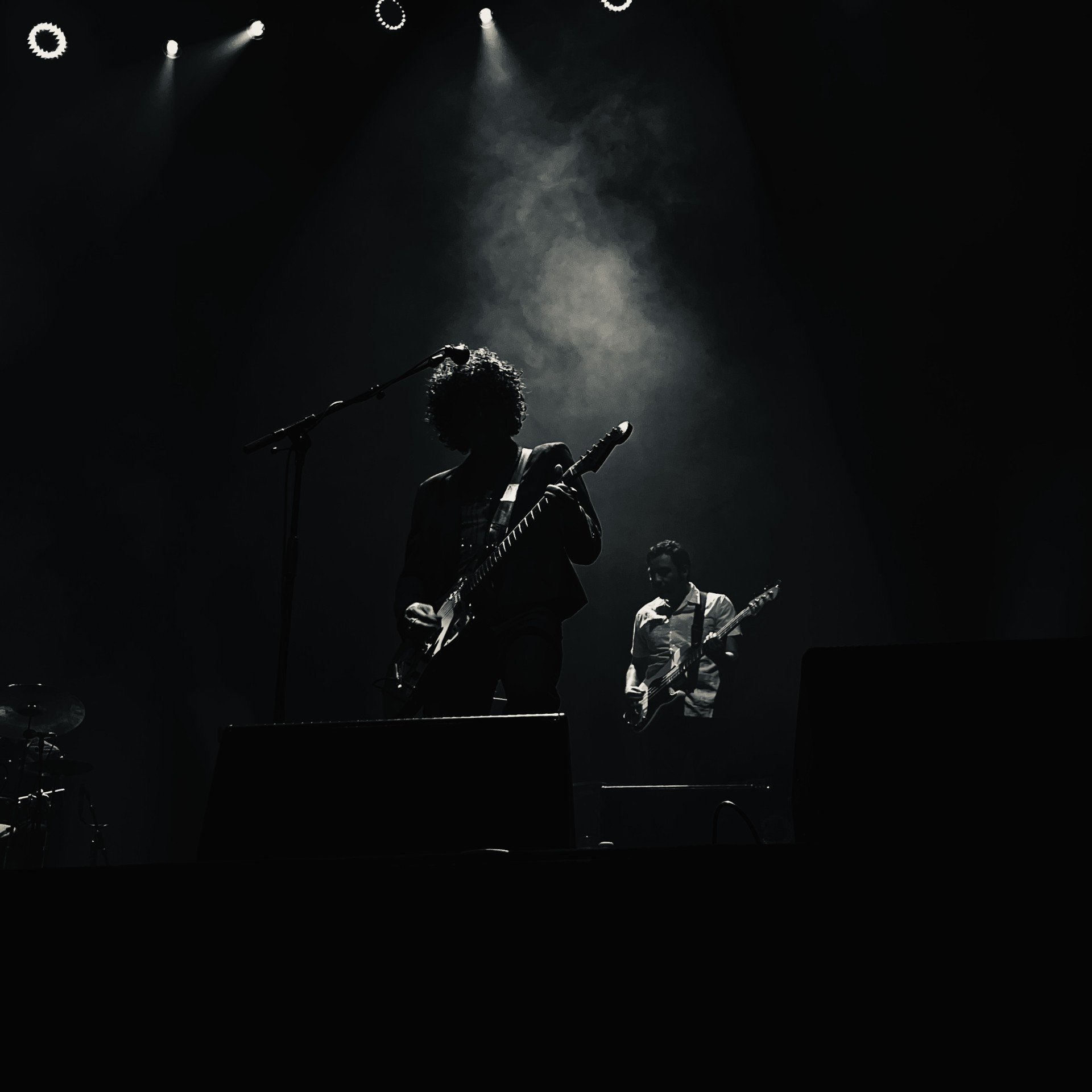 Silhouetted musicians performing on stage with guitars under dramatic spotlighting and smoke effects.