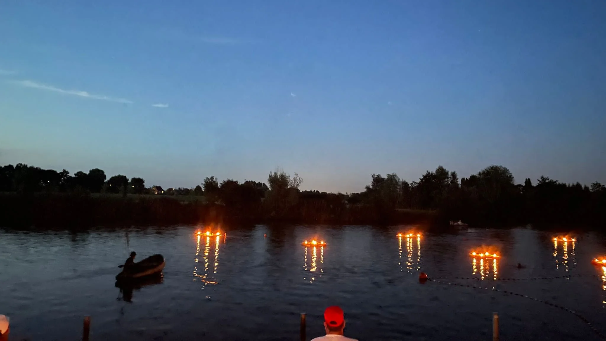 Een rivier bij zonsondergang met meerdere drijvende lantaarns en mensen in een boot. Bellenmolen, vuurmolen, onthaal, vuuranimatie, vuurspuwer, vuurartiest, vuurshow. Vuurvlotten.