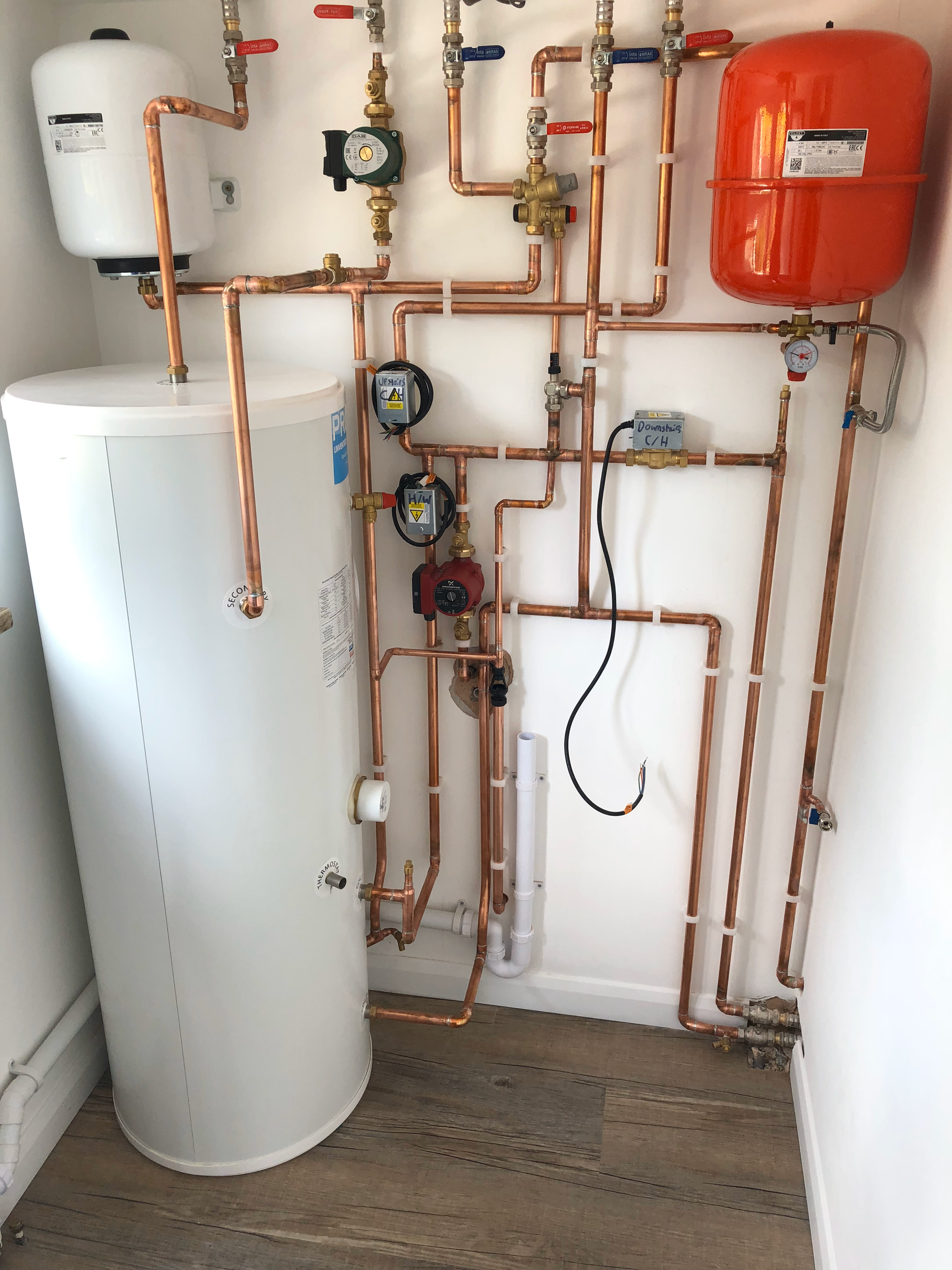 A water heater with a tank and an extensive network of copper pipes, gauges, and valves mounted in a utility room.