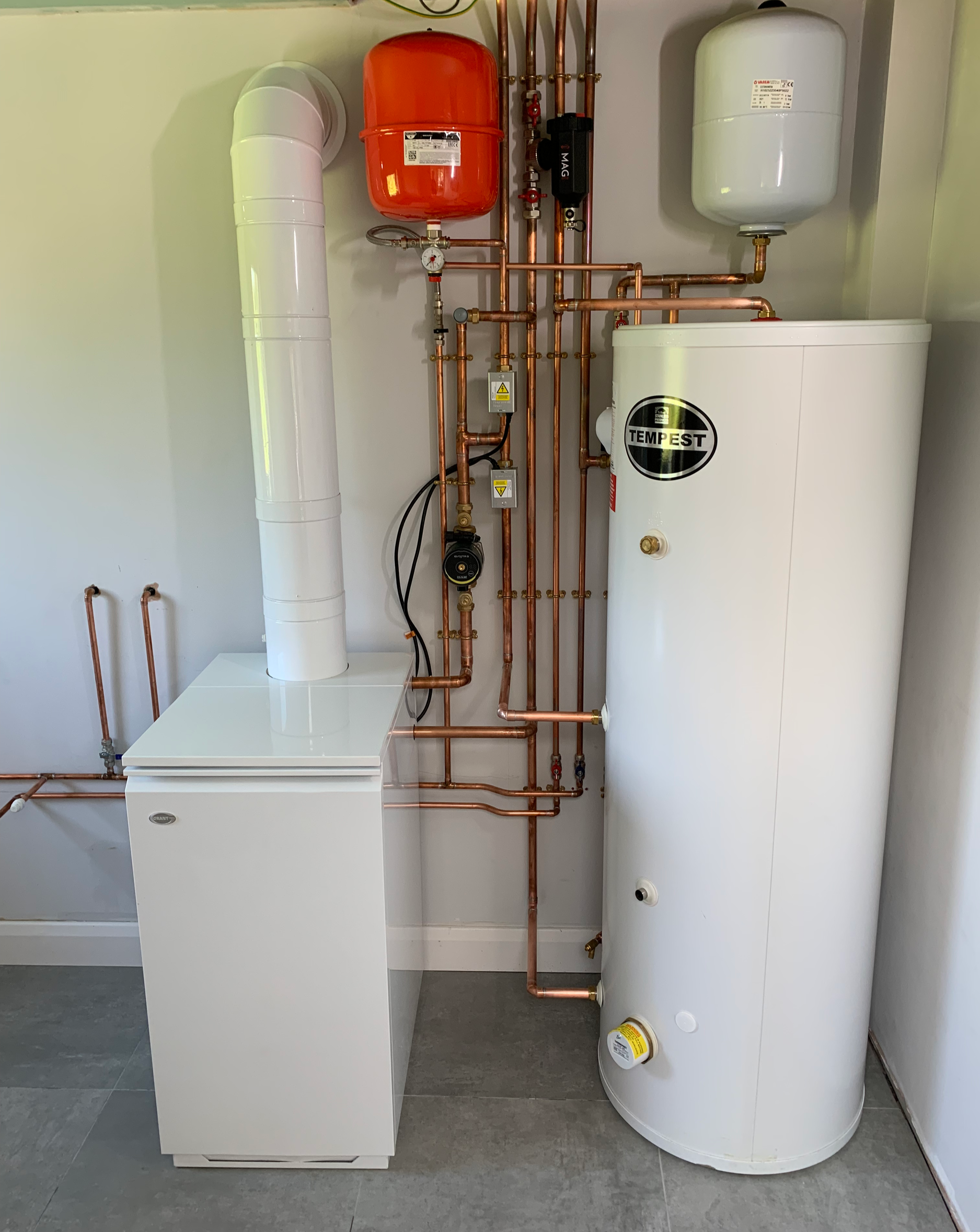 A water heating system workstation with copper pipes, a white tank labeled 'Tempest', a red expansion tank, and various gauges and controls.
