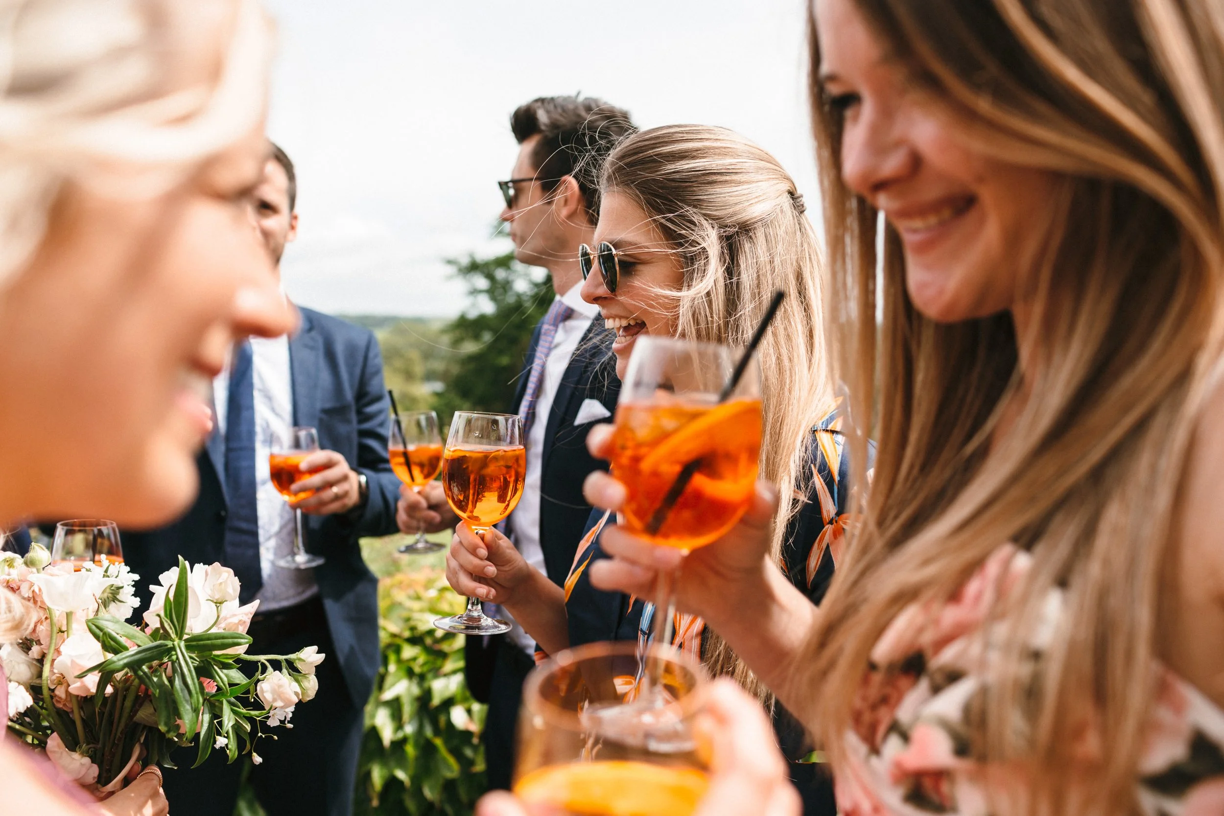 Wedding guests holding aperol spritz cocktails during wedding reception. Photographed by Freckle Photography.