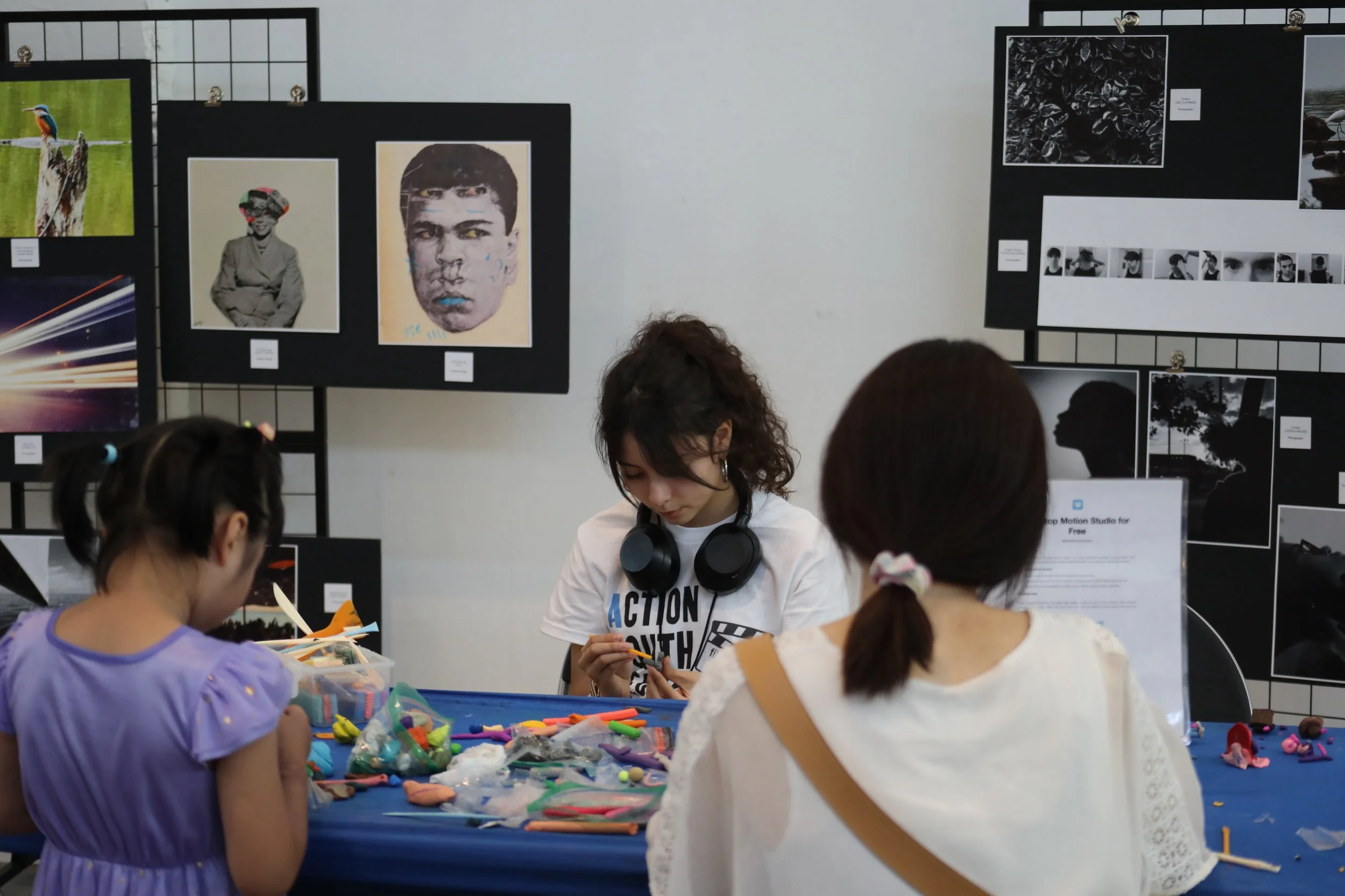 Three people sitting at a table and sculpting brightly colored clay. The pair facing away from the camera are an older woman and young child while the person across from them is an Action Youth Media employee.