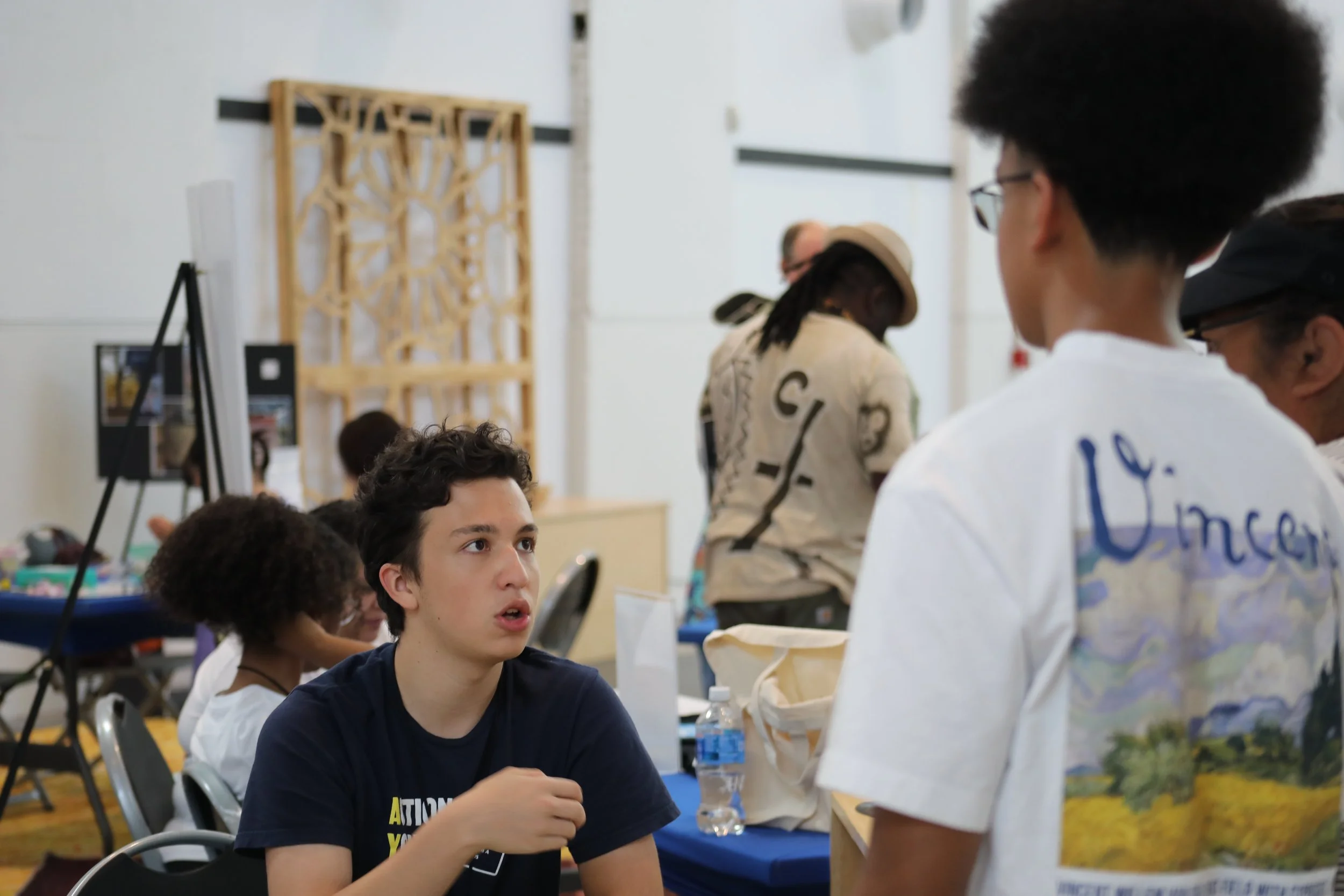 Two people talking. One is sitting down and wears an Action Youth Media shirt while the other is presumably a passerby.