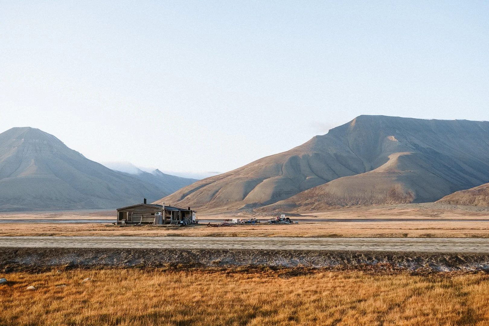 A rustic wooden house in an arid landscape with mountains in the background, under a clear sky.