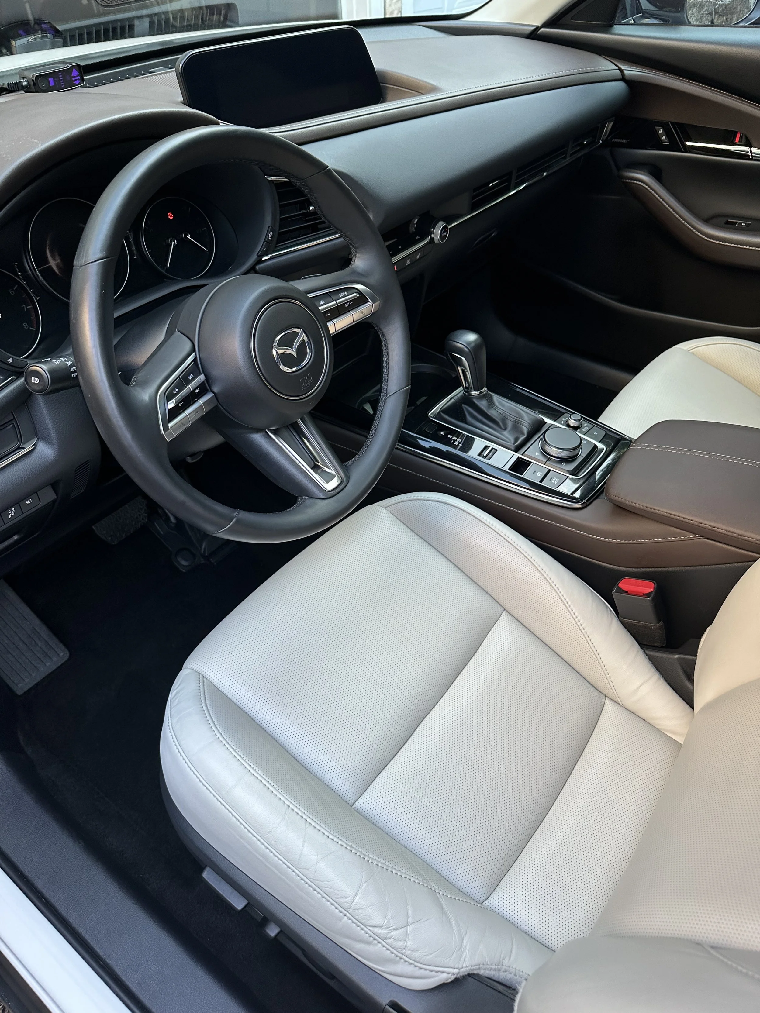 Inside the interior of a clean Mazda car, showing the steering wheel, dashboard, gear shift, and front seat.