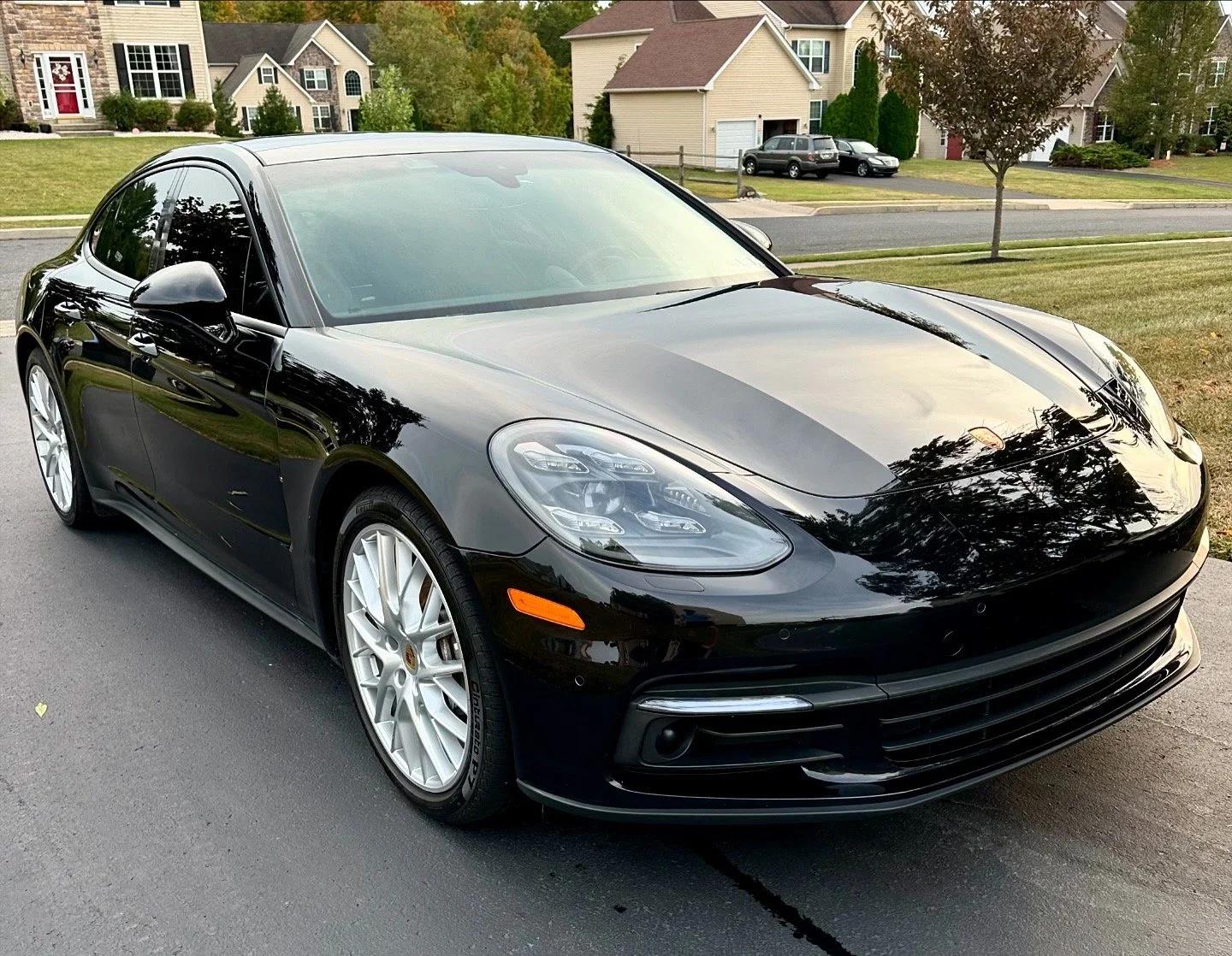 A black Porsche Panamera parked on a suburban street with houses and trees in the background