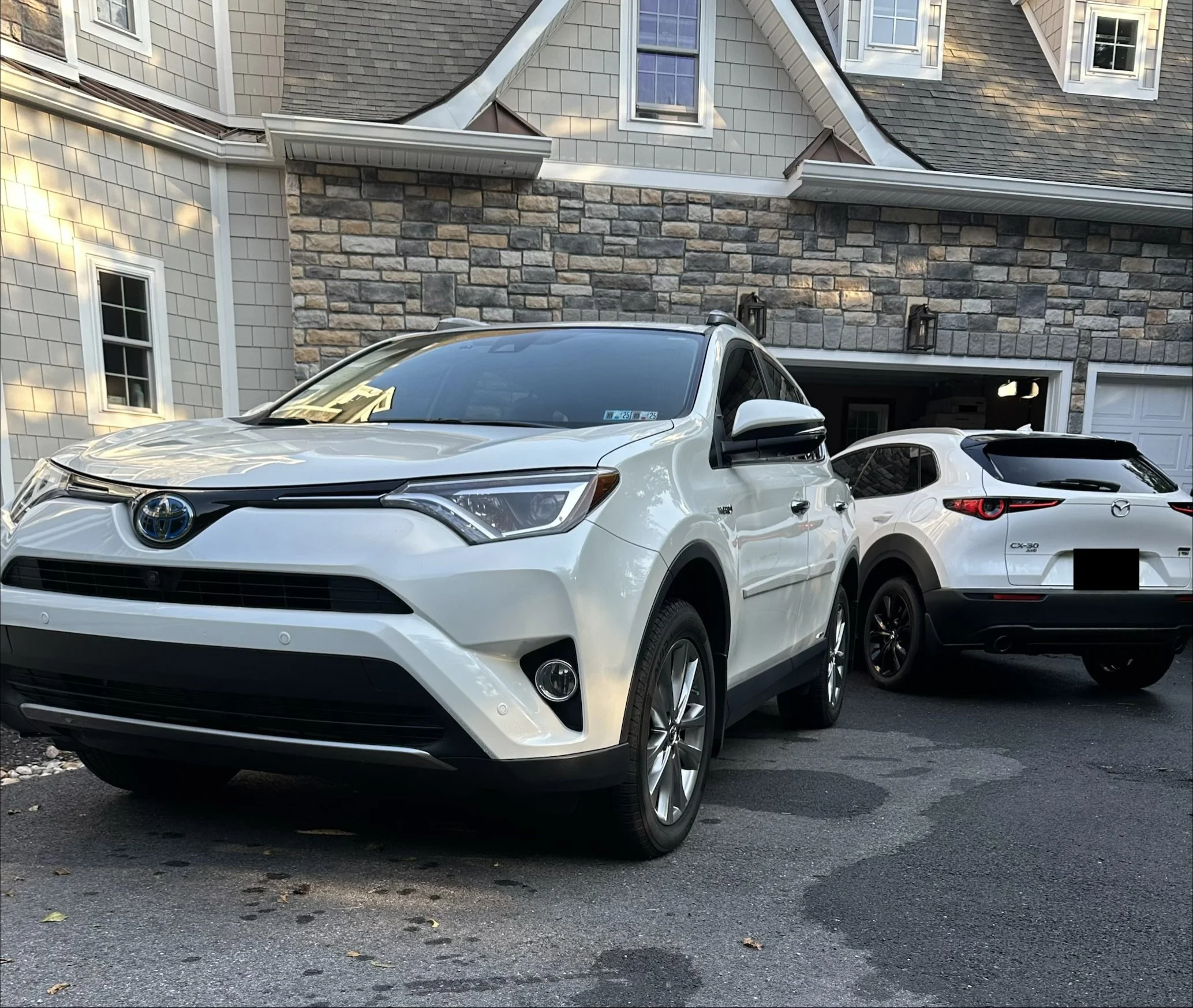 A white Toyota RAV4 parked in front of a house, with another white Mazda CX-30 parked behind it, in a residential driveway.