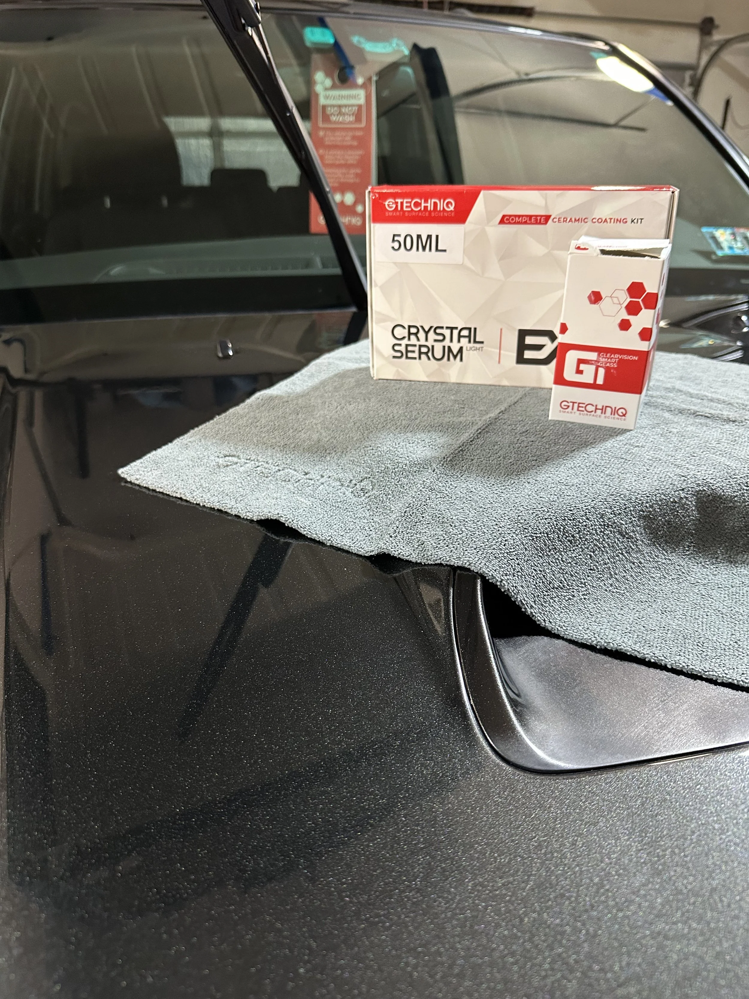 Box of Gtechniq Crystal Serum Light on a gray cloth on the hood of a black car with polish finish.