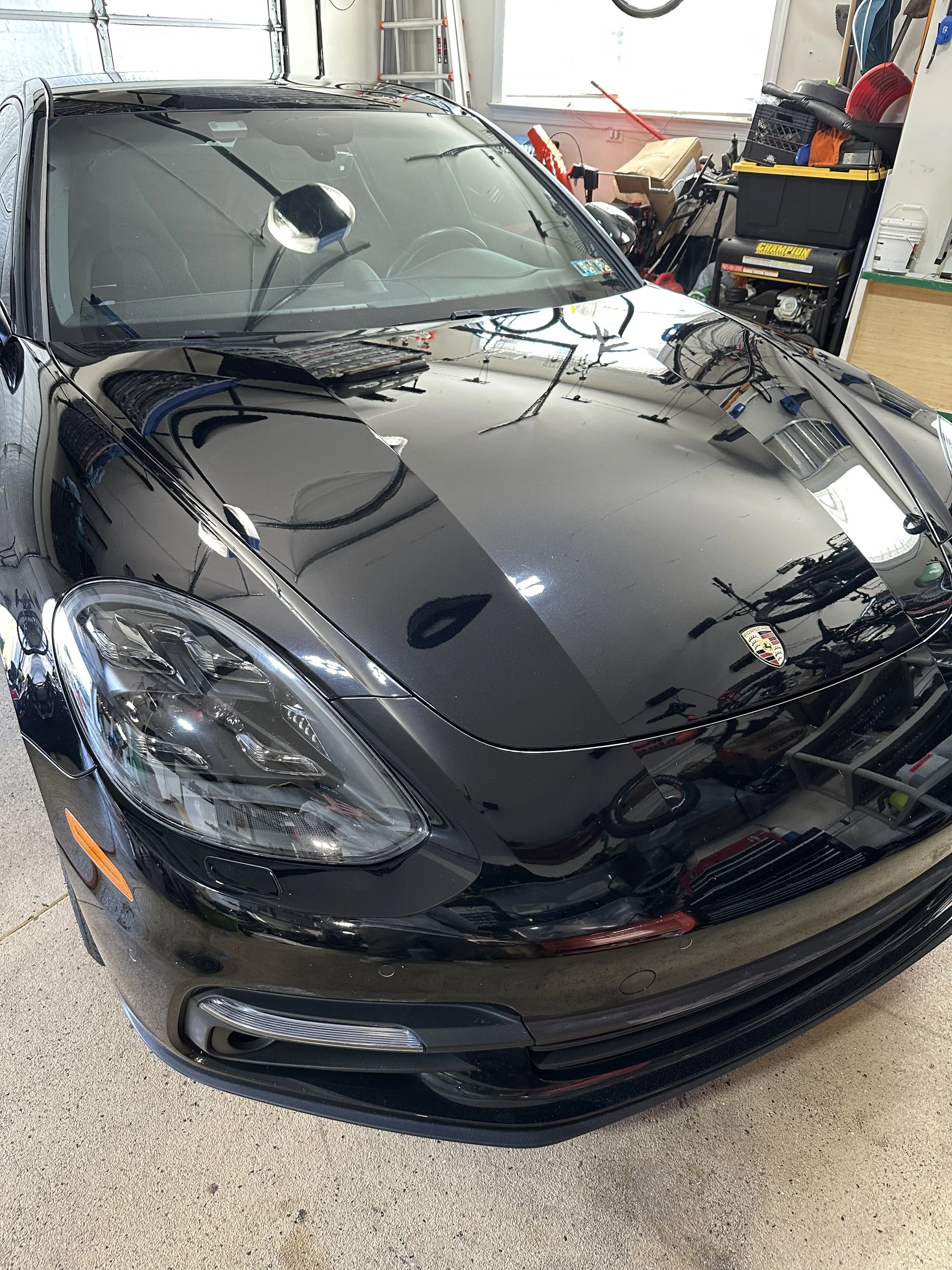 Polished Black Porsche sports car parked inside a garage with tools and supplies on shelves in the background.