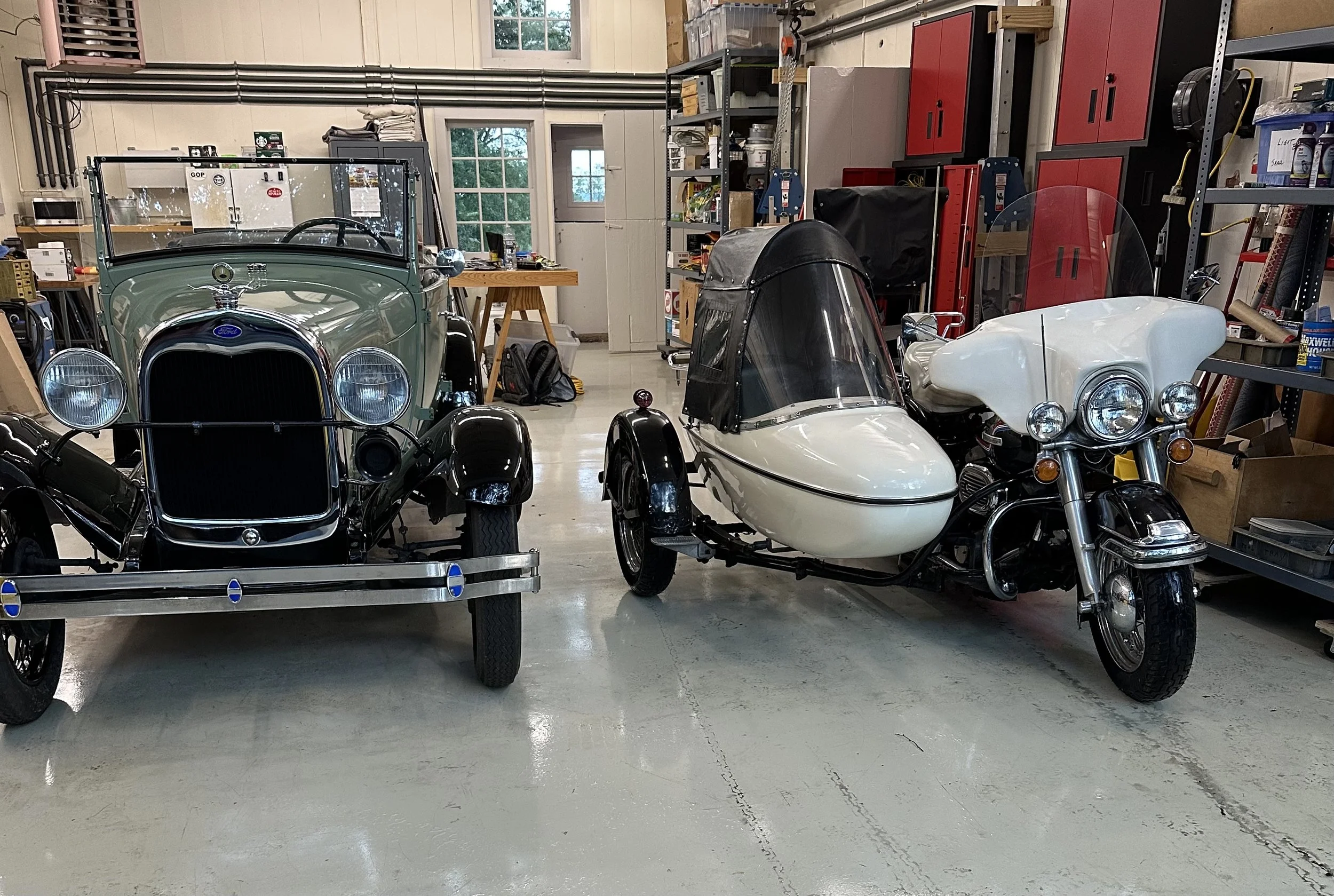A vintage green Ford automobile and a white motorcycle with a sidecar in a garage.