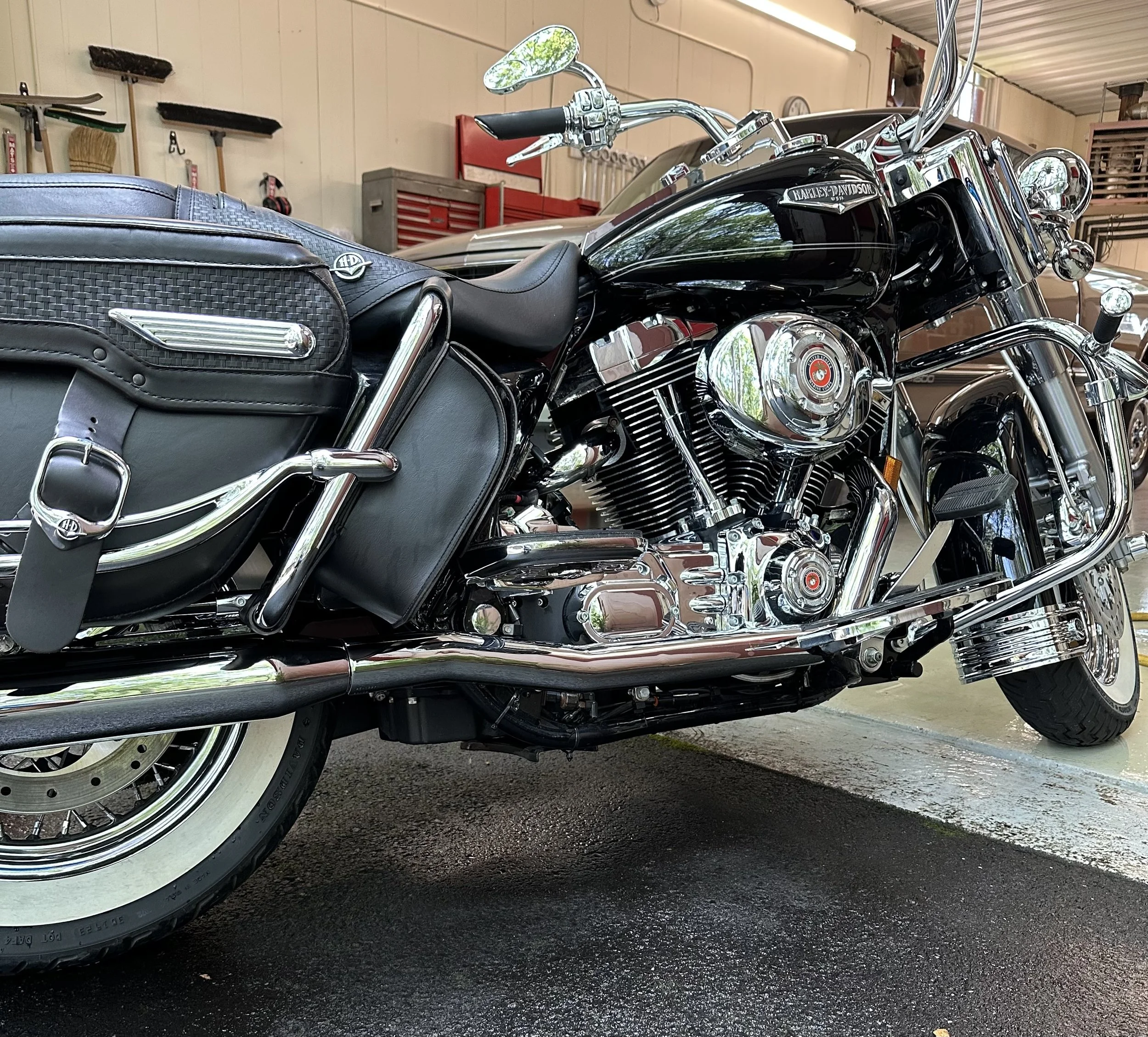 A clean black and chrome Harley-Davidson touring motorcycle parked indoors, with leather saddlebags and chrome accents.
