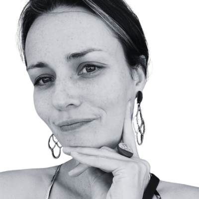 Black and white photo of a woman with earrings, resting her chin on her hand and smiling softly.