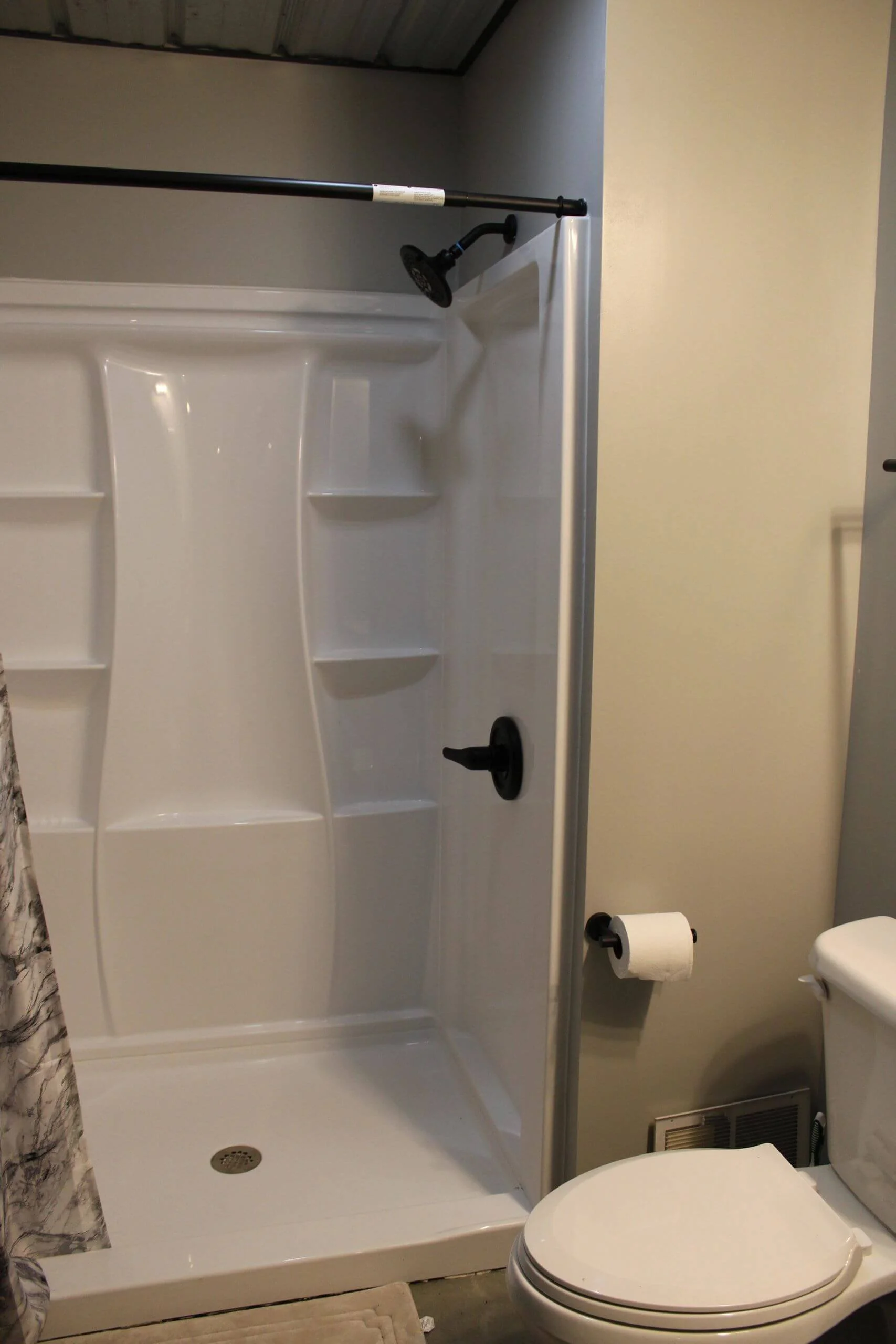 Bathroom with a white shower stall, black showerhead, toilet, toilet paper roll, and a vent on the wall.