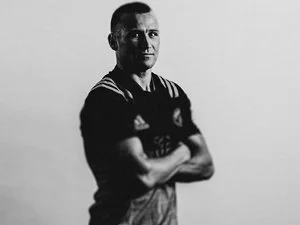 Black and white portrait of a person in a sports jersey with arms crossed, looking at the camera.