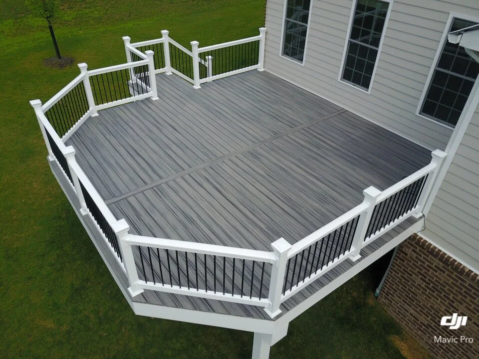 Elevated wooden deck with white railings attached to a house, surrounded by green grass.