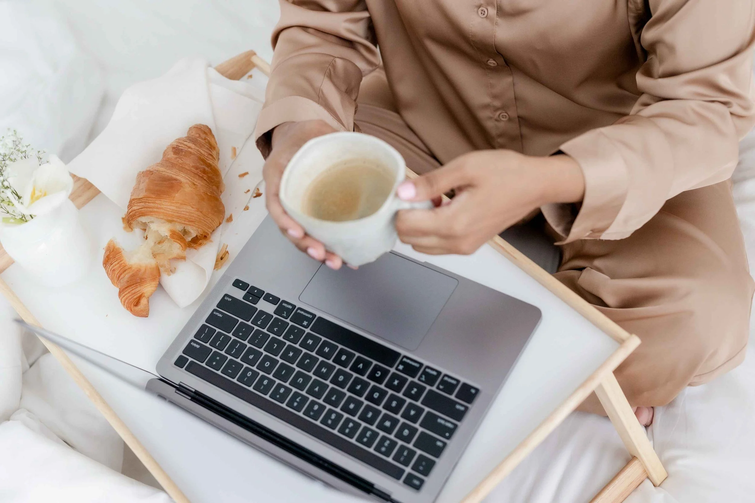 A woman working on Pinterest strategy for wedding photographers with coffee and a croissant by her side.