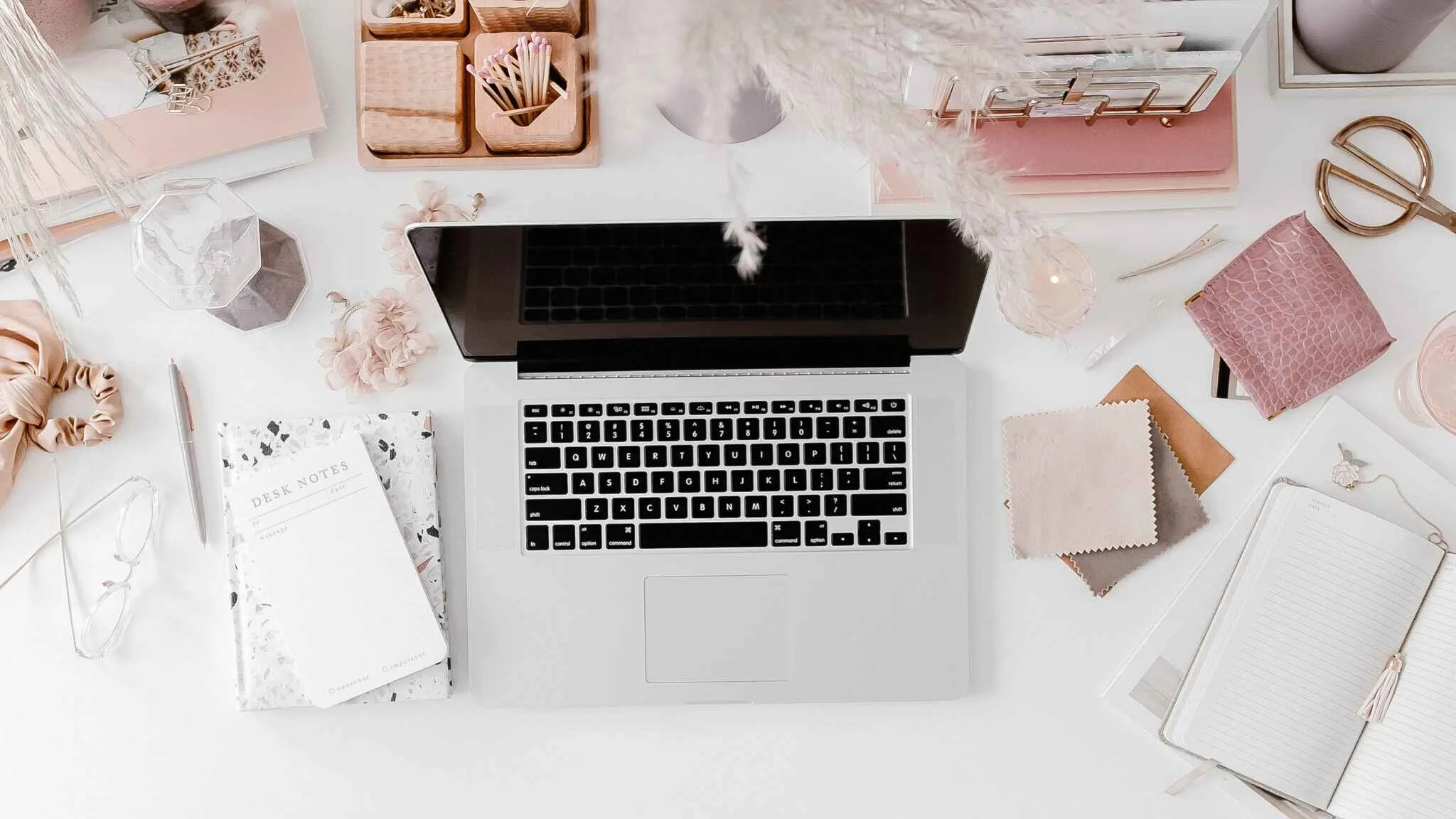 A stylish desk setup with a laptop, notebook, and planner for wedding creatives.