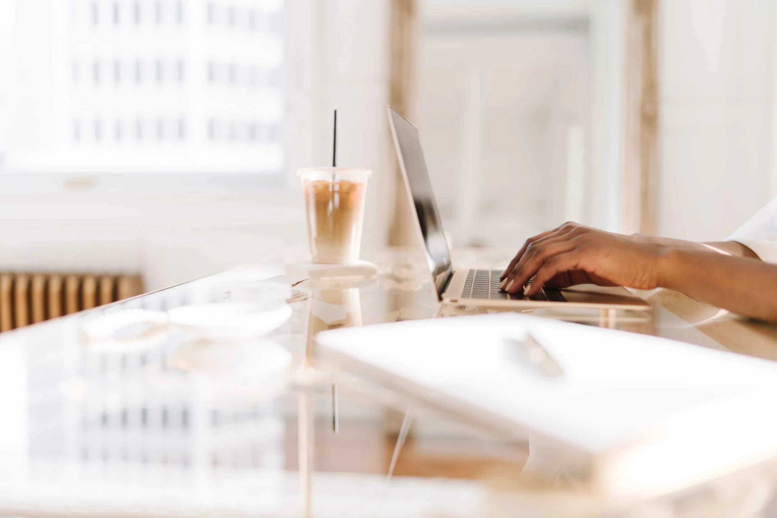 Hands typing on a laptop with an iced coffee, ideal for Pinterest blogging setup.