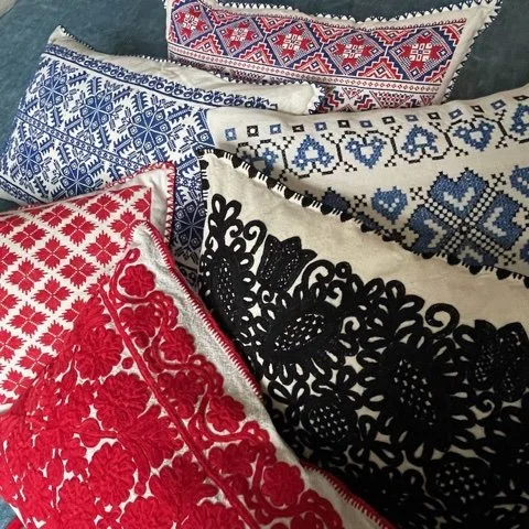 Multiple embroidered textile pieces with intricate patterns in red, black, white, and blue colors, overlapping each other.