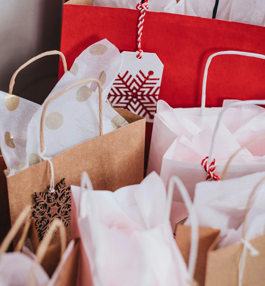 Multiple Christmas gift bags in red, white, and brown with holiday decorations such as snowflake ornaments and a holiday tag.