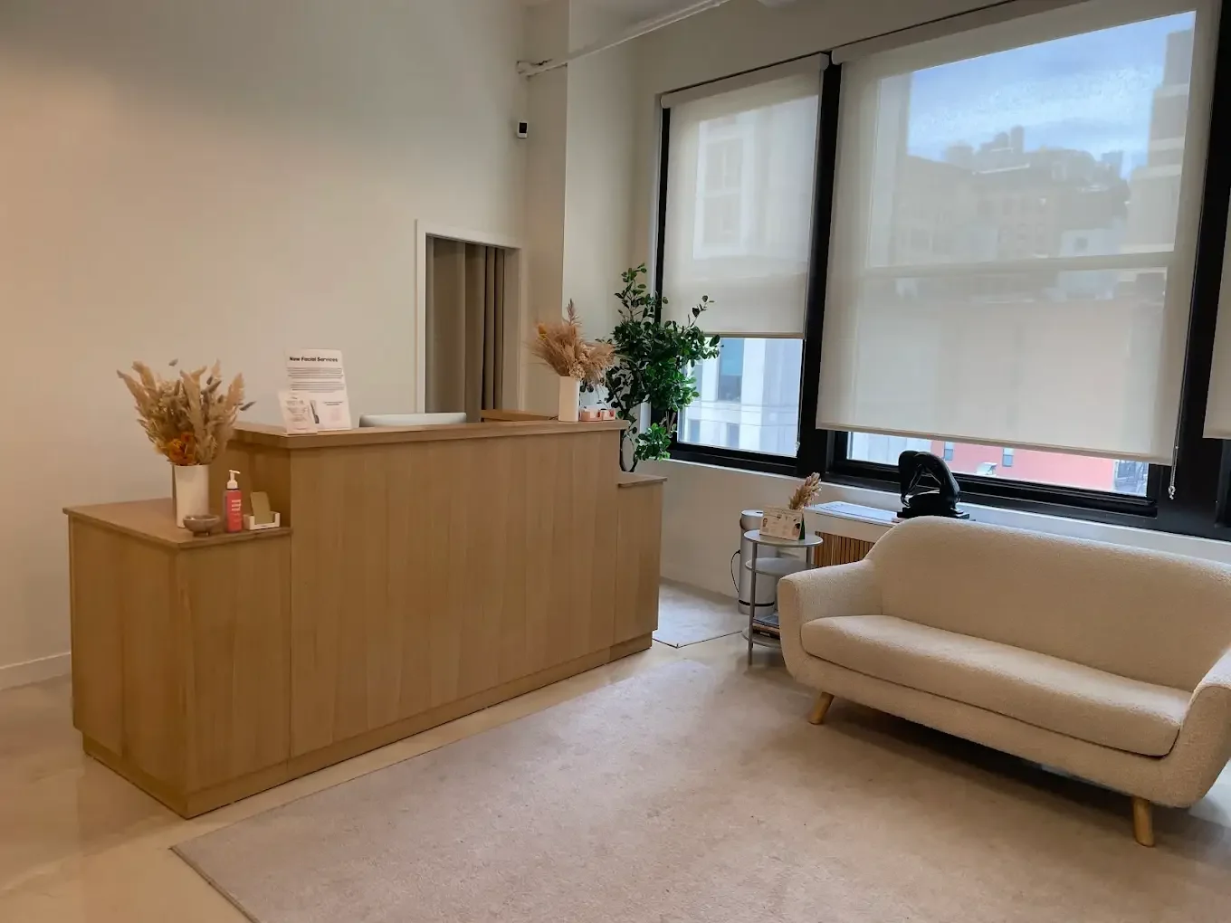 A beige ceramic vase with dried branches on a wooden surface, with sunlight casting shadows on a plain wall.
