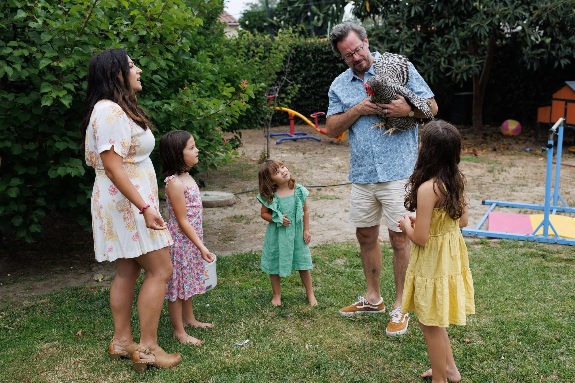 Mom and three daughters look on as Dad holds chicken that's flapping its wings. Photo by Shannon Fisher, an Orange County family photographer.