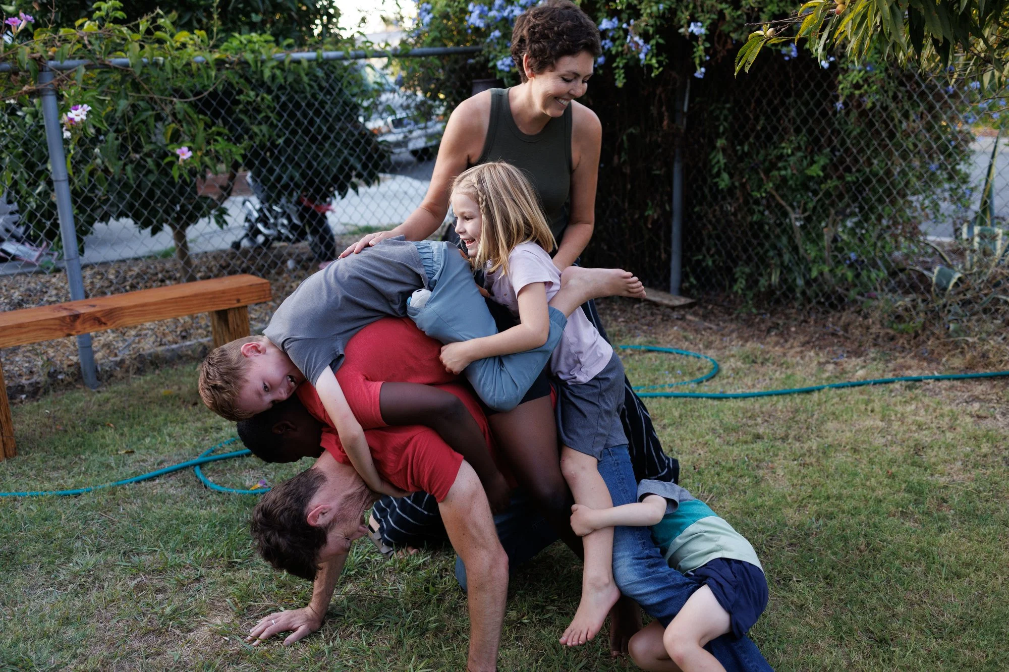 Holiday card photographer: Four kids pile on top of their dad in the backyard while mom steadies them
