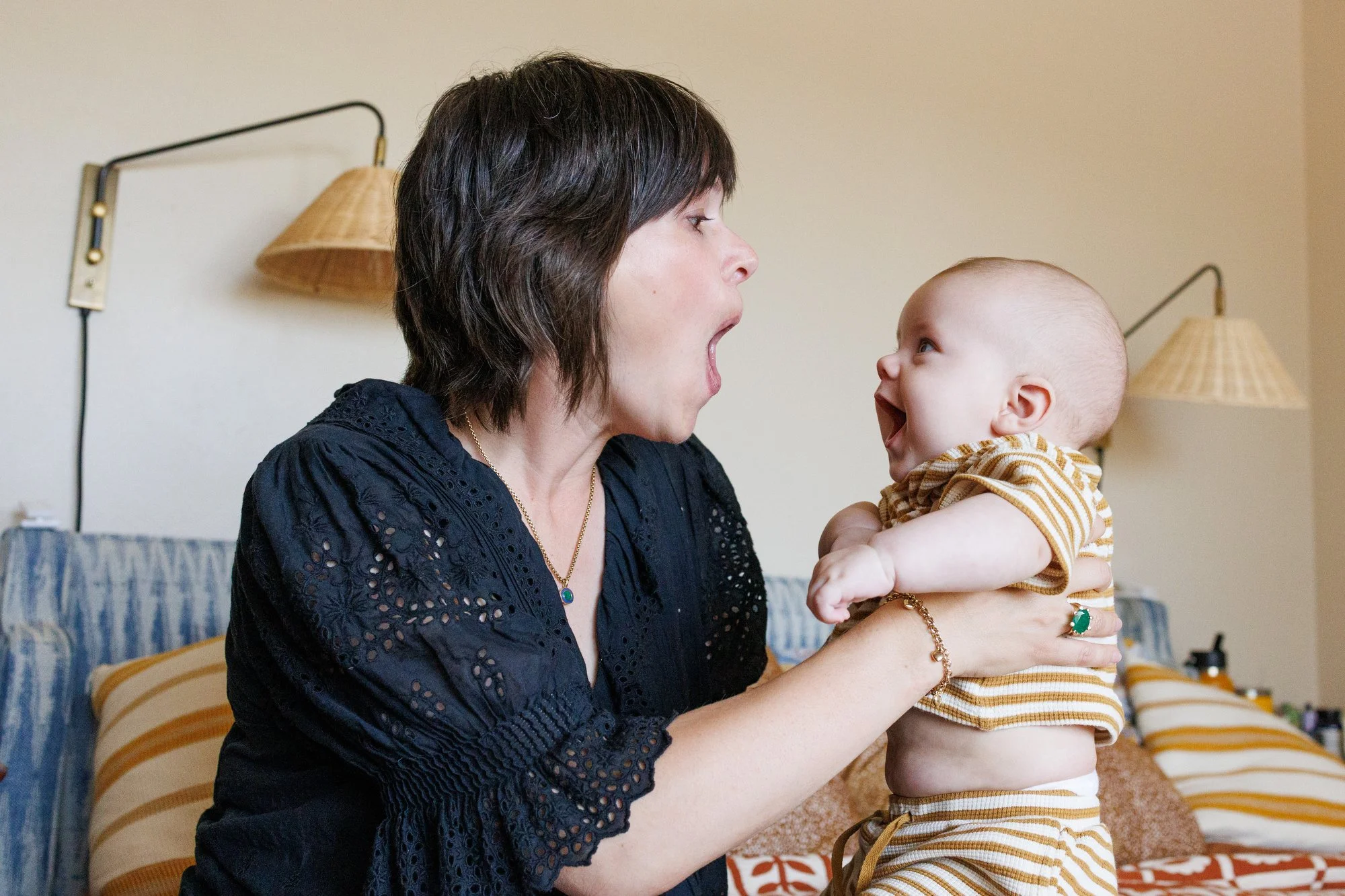In an in-home photography session by Shannon Fisher, Mom holds her baby up to her eye level and opens her mouth wide at him. Baby mimics her expression, looking bright-eyed.