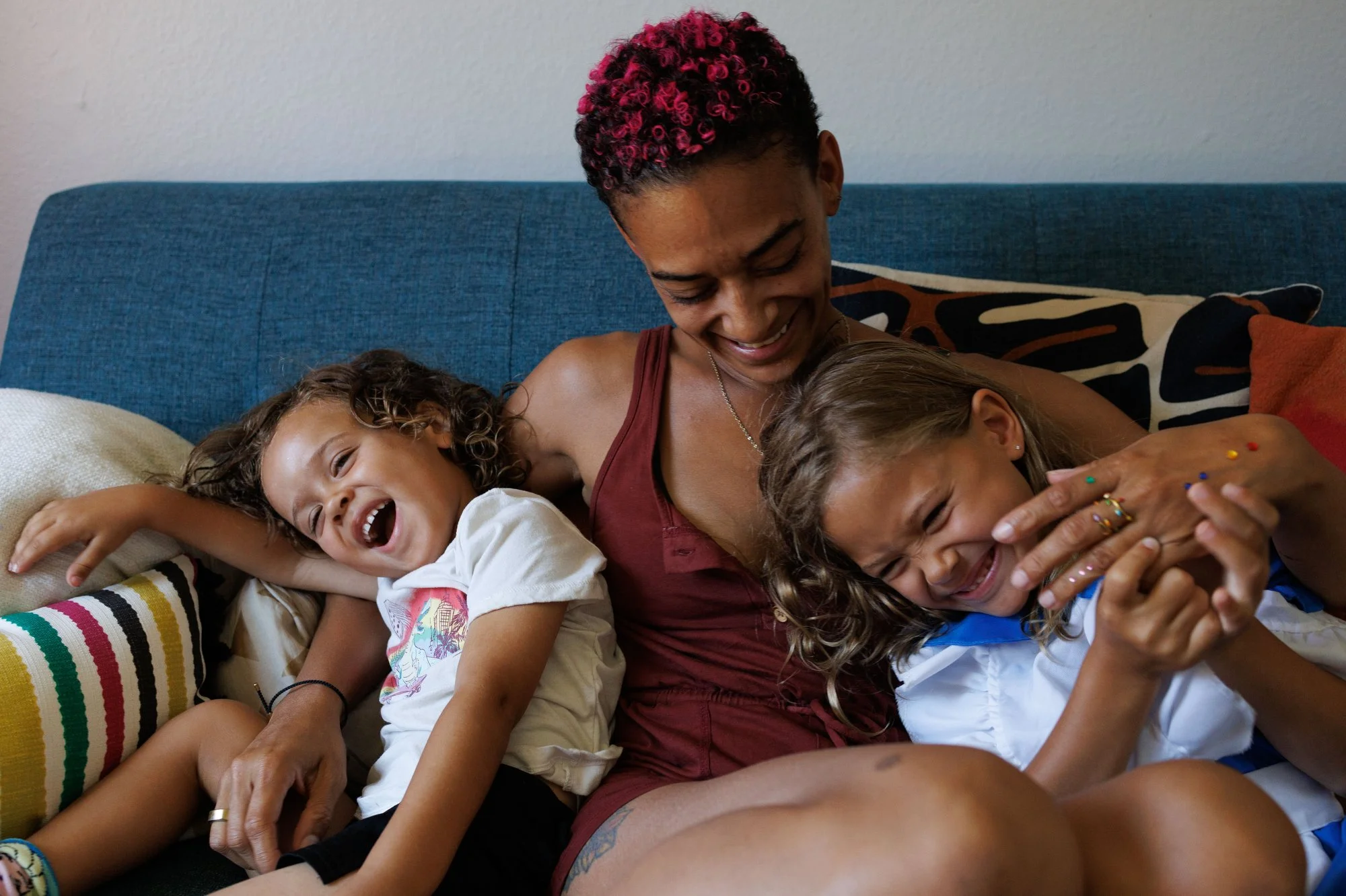 holiday card photographer: a mom with pink highlighted curly hair and her two kids laughing on a couch
