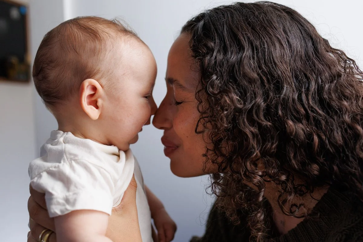 Mom touches noses to her baby. She has her eyes closed and smiles. The baby smiles too.