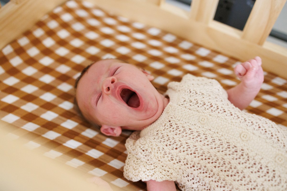 Newborn in crocheted onesie yawns while laying on a plaid cribsheet in Orange County newborn photography session by Shannon Fisher Photo