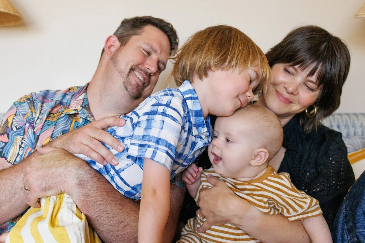 Older brother cuddles into baby brother, with mom and dad holding the two of them. Photo by Shannon Fisher Photo, an OC family photographer