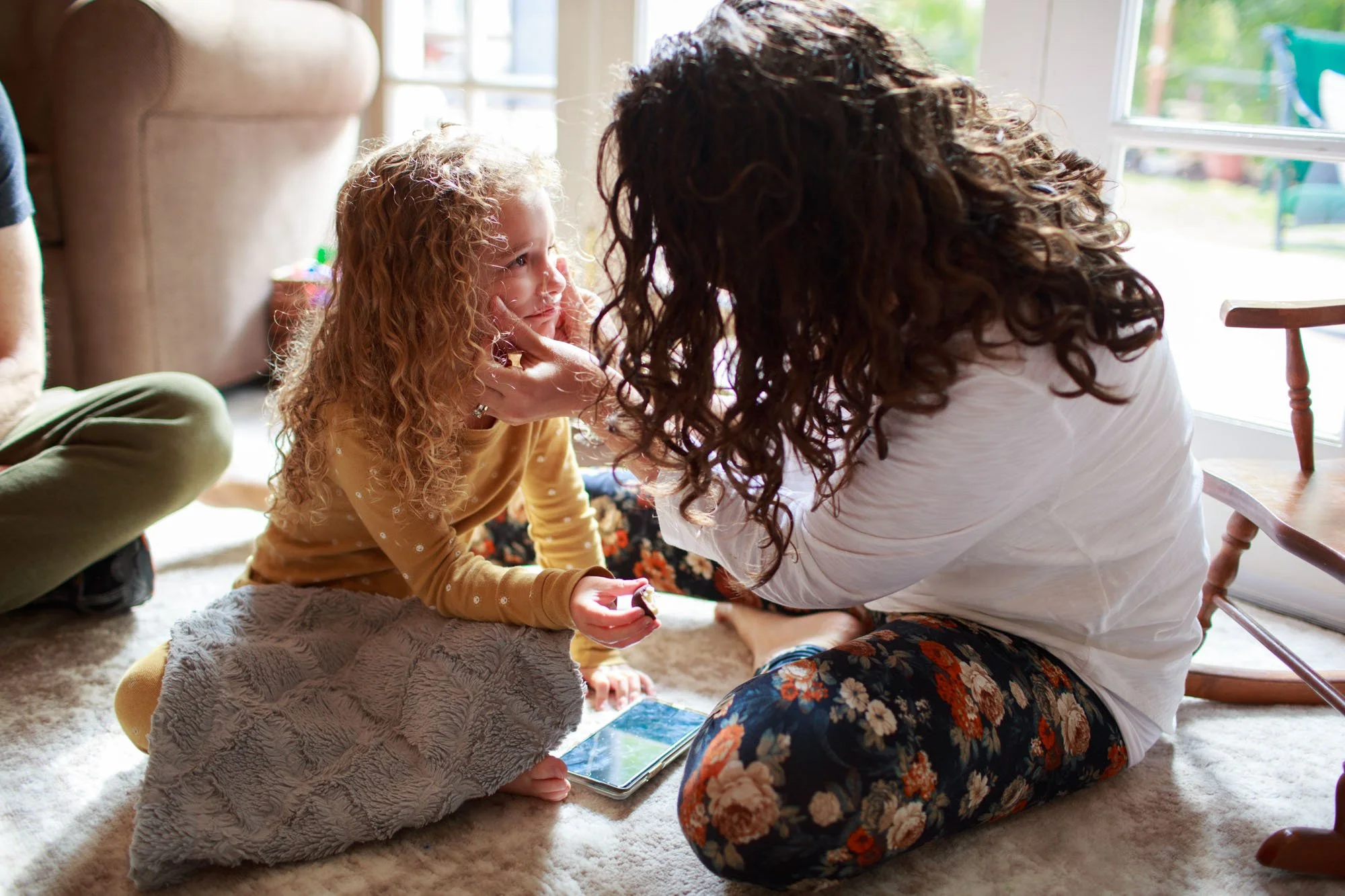 A little girl gets her tears wiped by her mom. She holds a piece of chocolate. In-home maternity and family photography by Shannon Fisher.