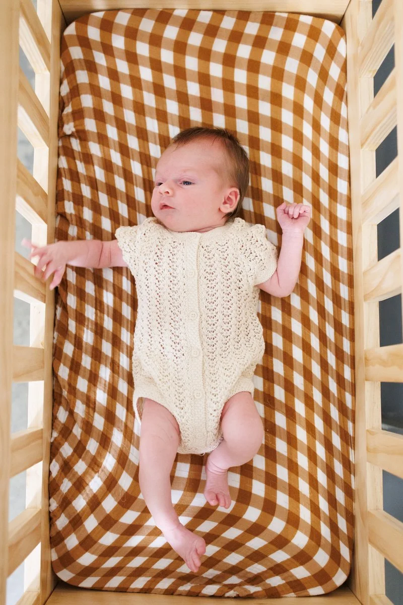 Baby in crochet onesie lays on a plaid sheet in his crib