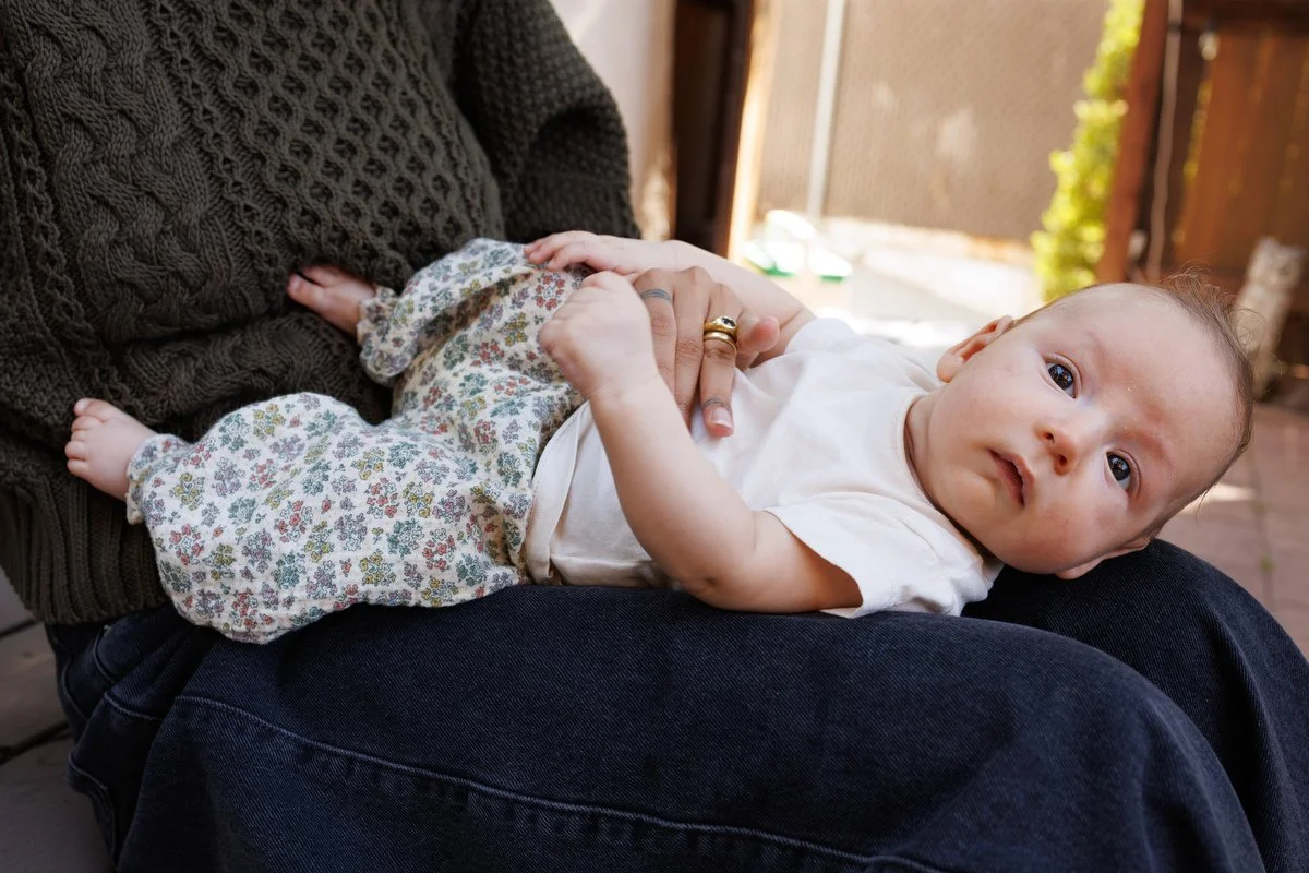 Alert 12-week-old baby looks into the camera while laying on mom's lap. Photo by Shannon Fisher Photo, an OC newborn photographer.