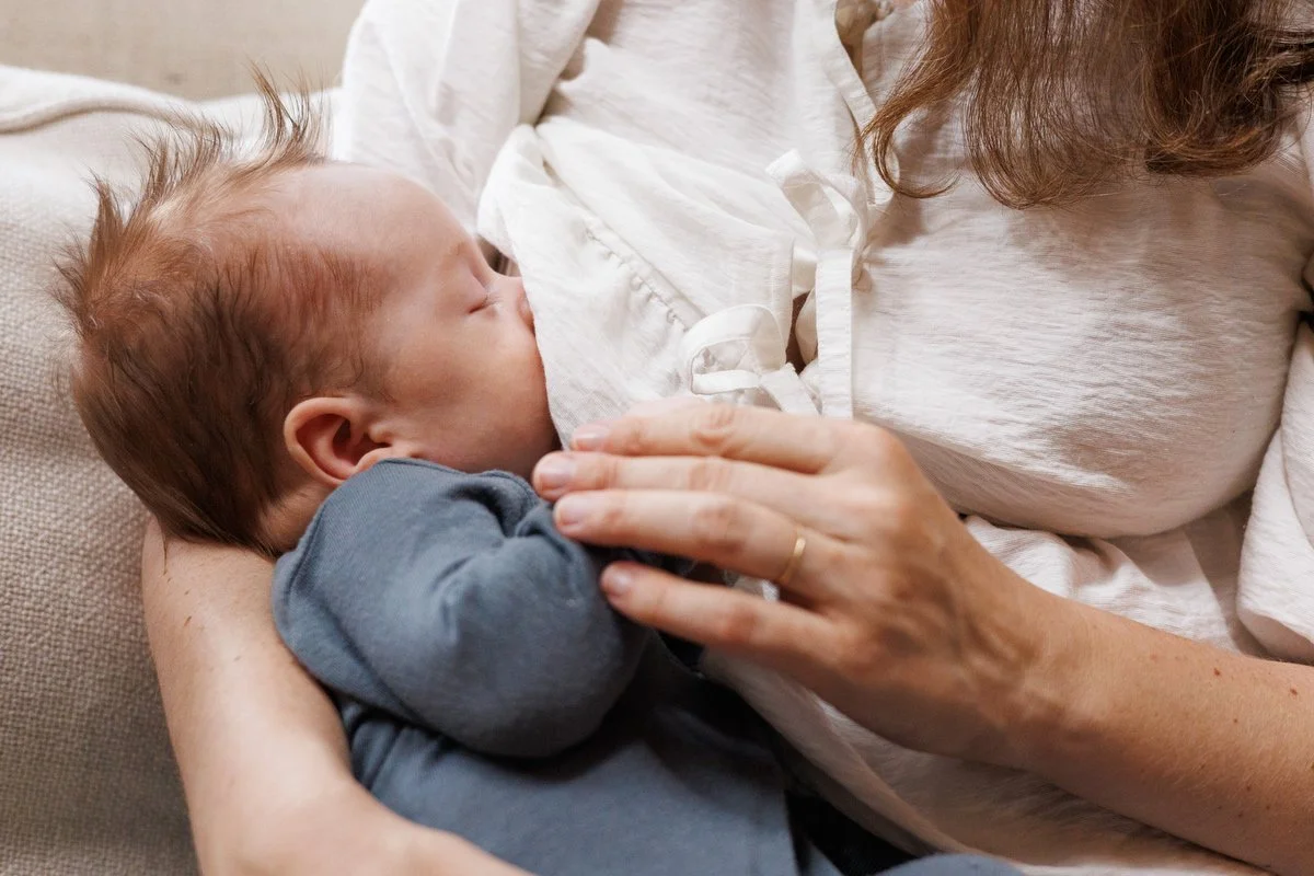 Baby with hair sticking straight up breastfeeds as Mom places a hand on his arm. Photo by Shannon Fisher