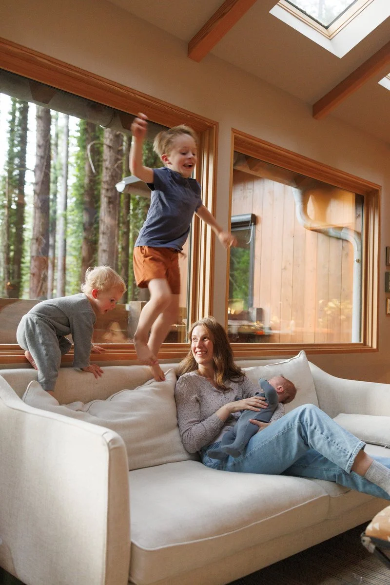 Older siblings jump on couch while mom holds newborn son in Orange County newborn photography session by Shannon Fisher Photo