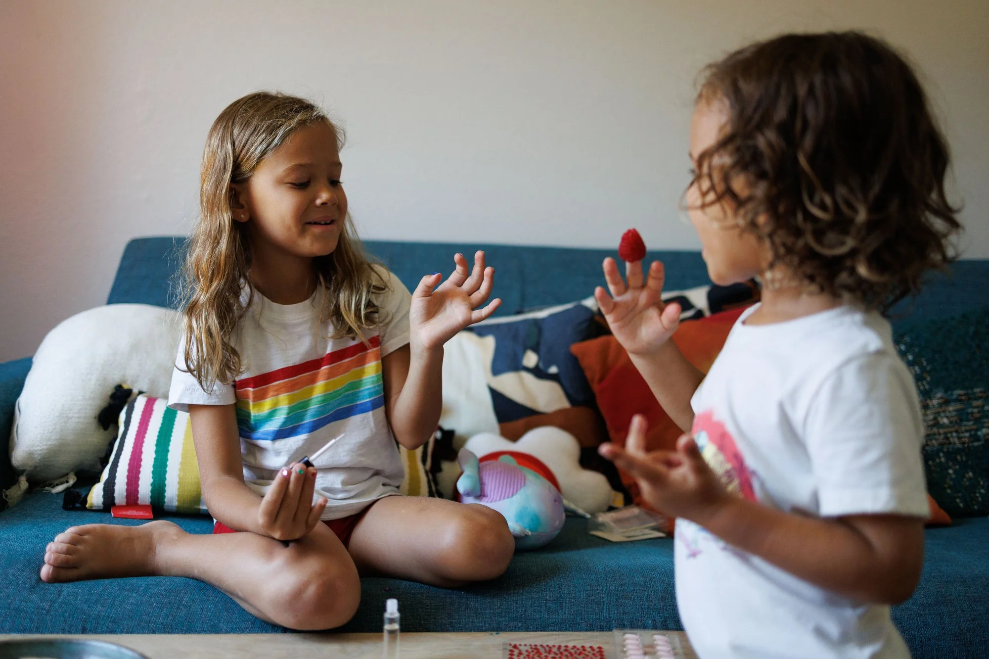 Two little girls in rainbow shirts talk, one has a raspberry on her fingertip. Photo by Shannon Fisher, an Orange County newborn and family photographer.