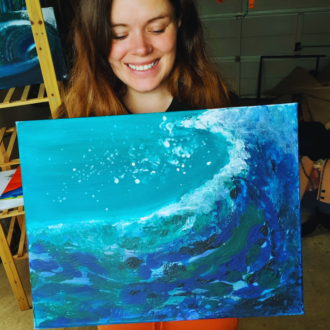 Woman smiling and holding an abstract painting of a wave in shades of blue and white.