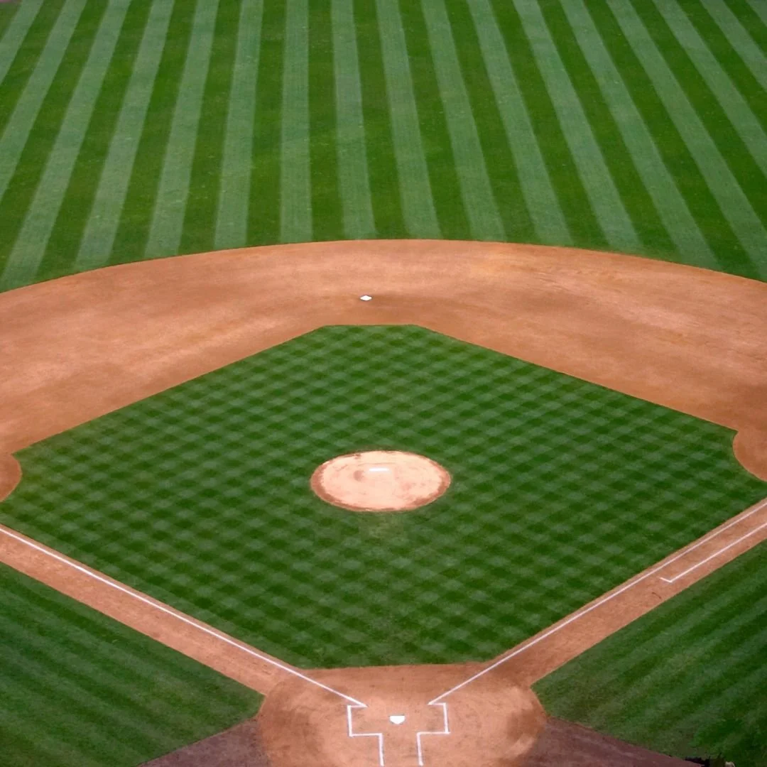 Empty baseball field with green grass and brown infield, viewed from above.