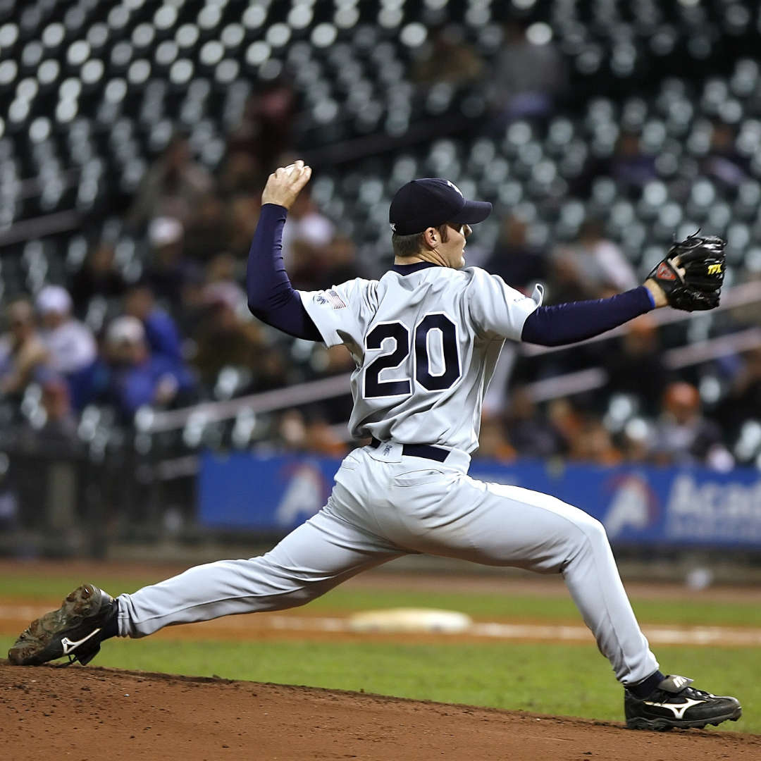 Baseball pitcher in a gray uniform, number 20, throwing a pitch on a baseball field with empty stadium seats in the background.