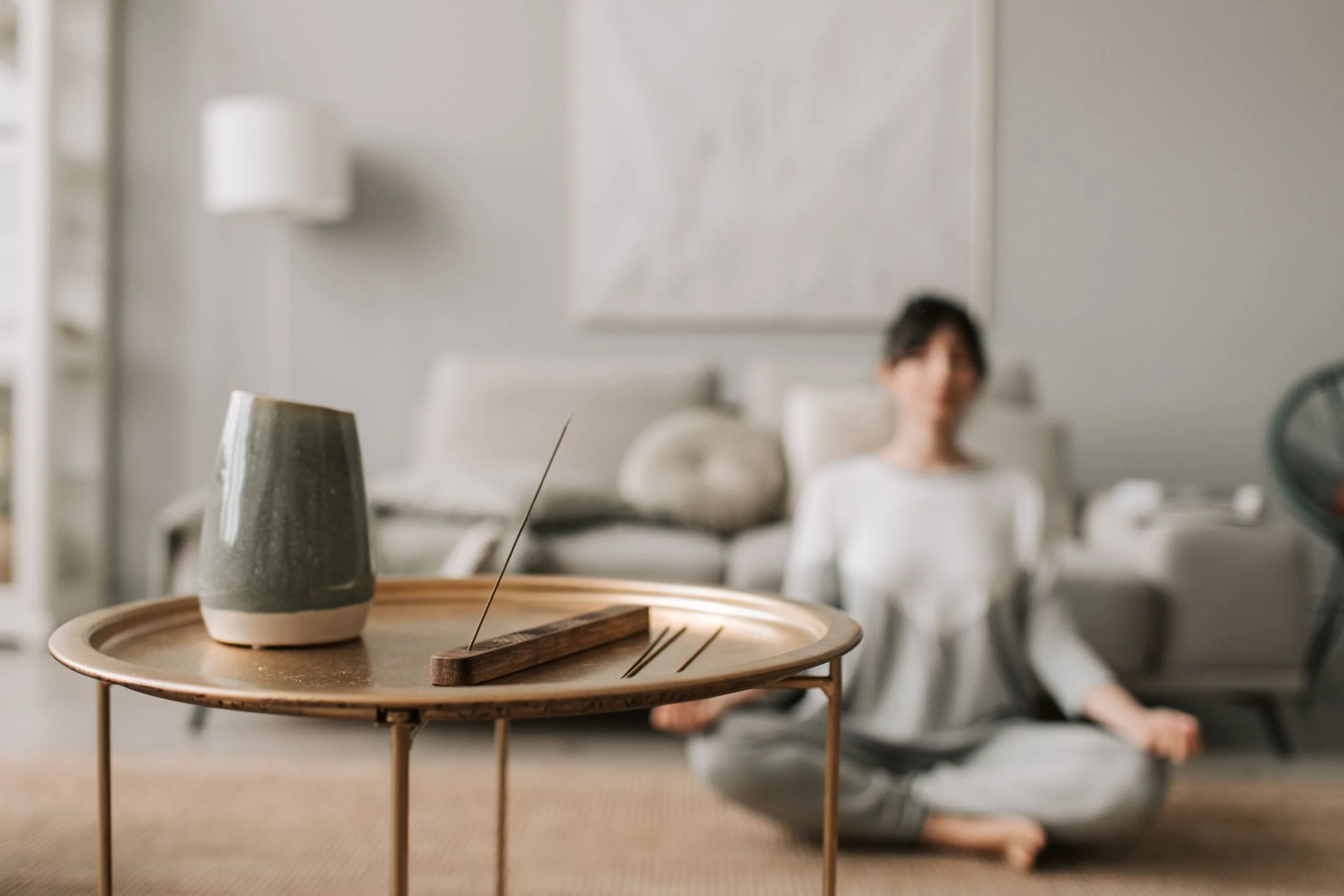 A small ceramic cup on a wooden tray with incense sticks in a cozy, minimalist room.