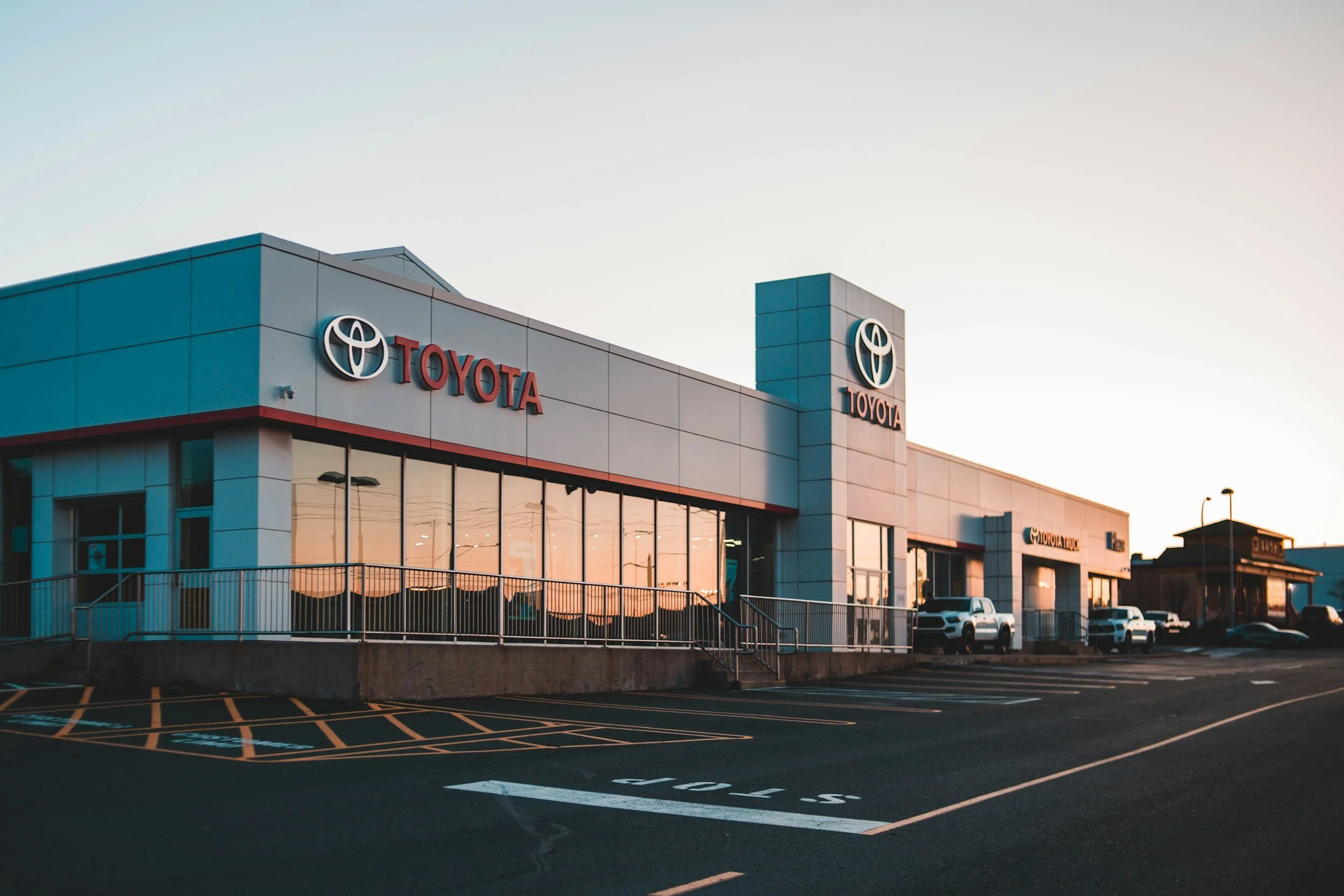 Exterior of a Toyota car dealership during sunset with a parking lot in the foreground.